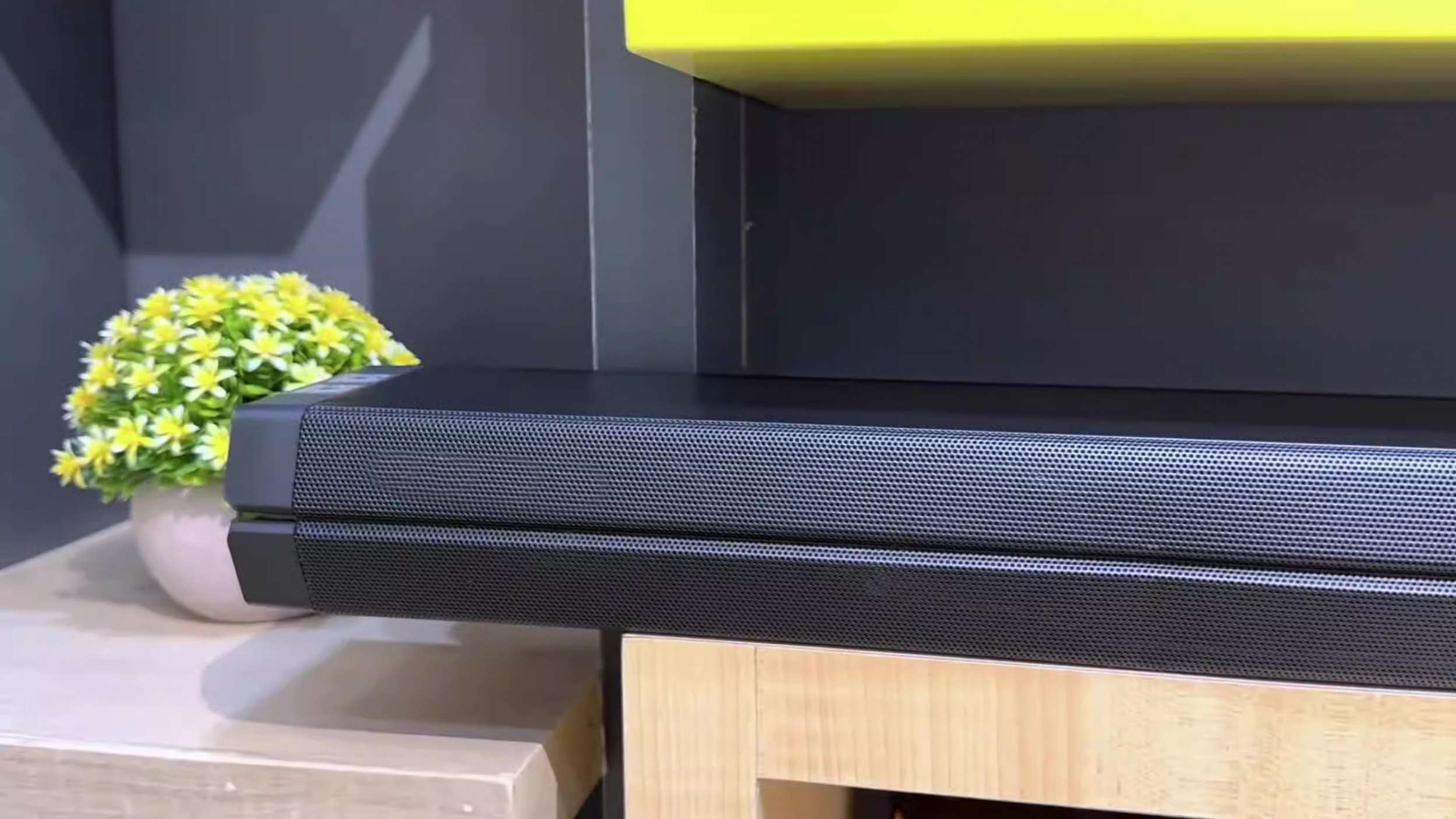 Soundbar auf Holzständer mit einer Vase gelber Blumen.