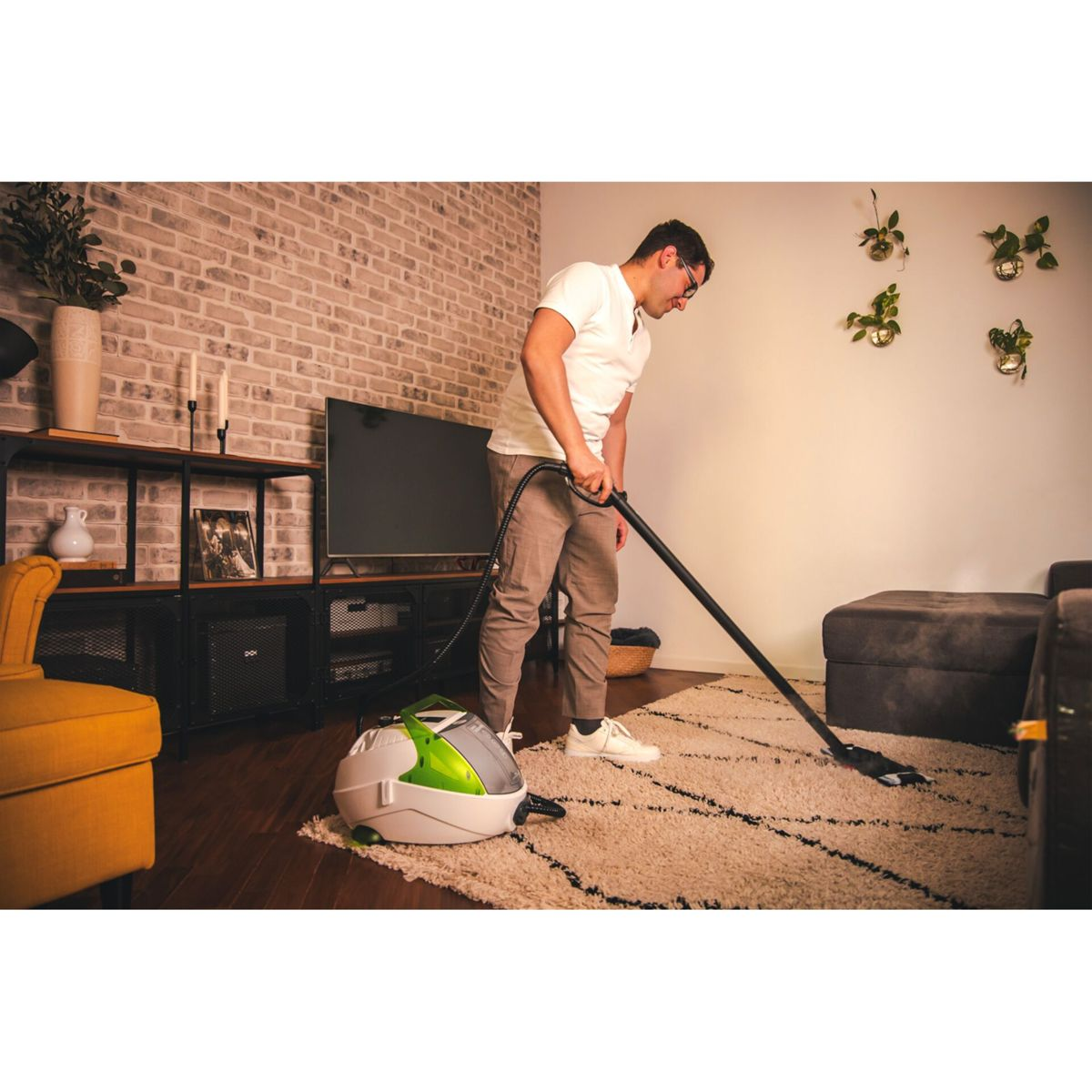 Mężczyzna odkurza dywan w salonie. Odkurzacz parowy jest na pierwszym planie.