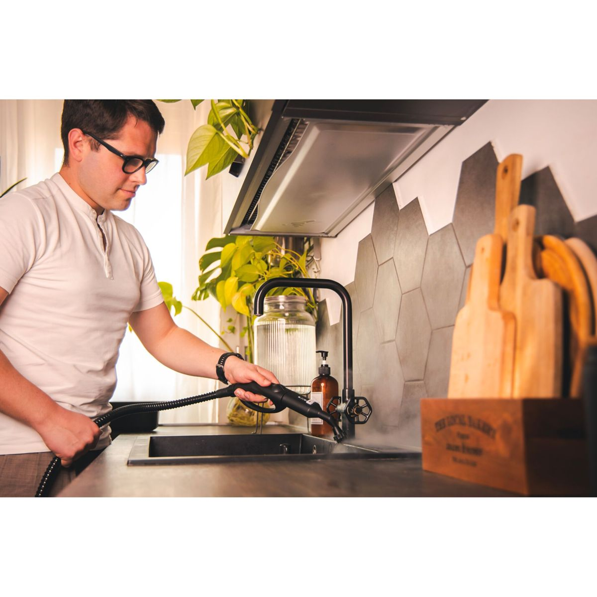 Mężczyzna używa parownicy w kuchni. Czyści blat. Szklany słoik i drewniana skrzynka po prawej.