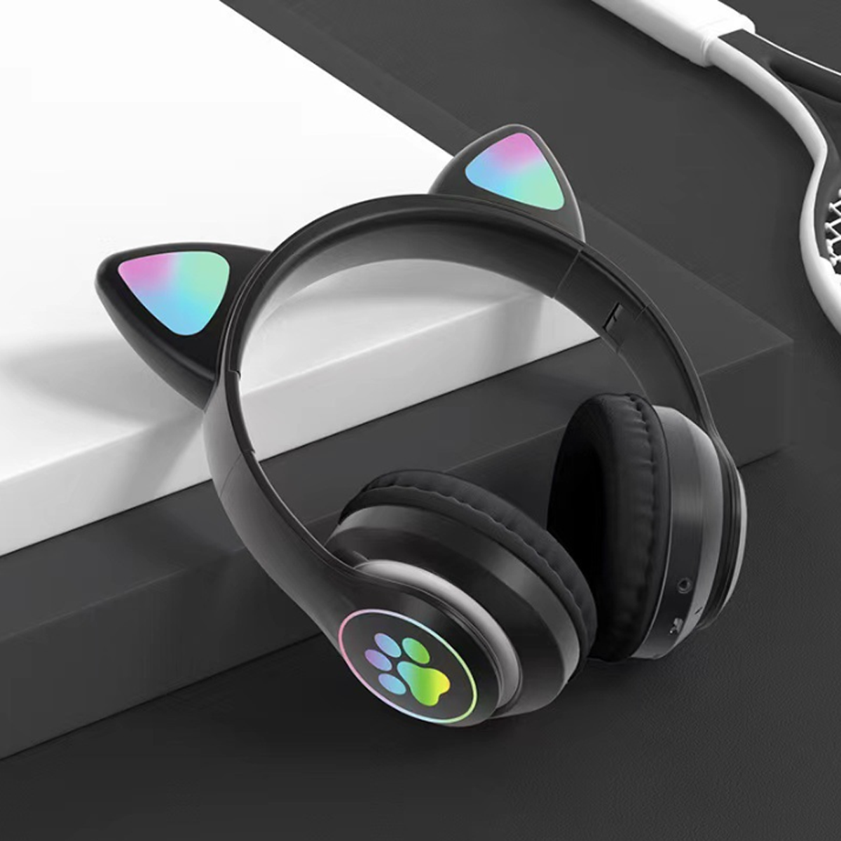 Schwarze Katzenohrkopfhörer mit Regenbogenlichtakzenten, Pfotenabdruck an der Seite, vor dunklem Hintergrund.