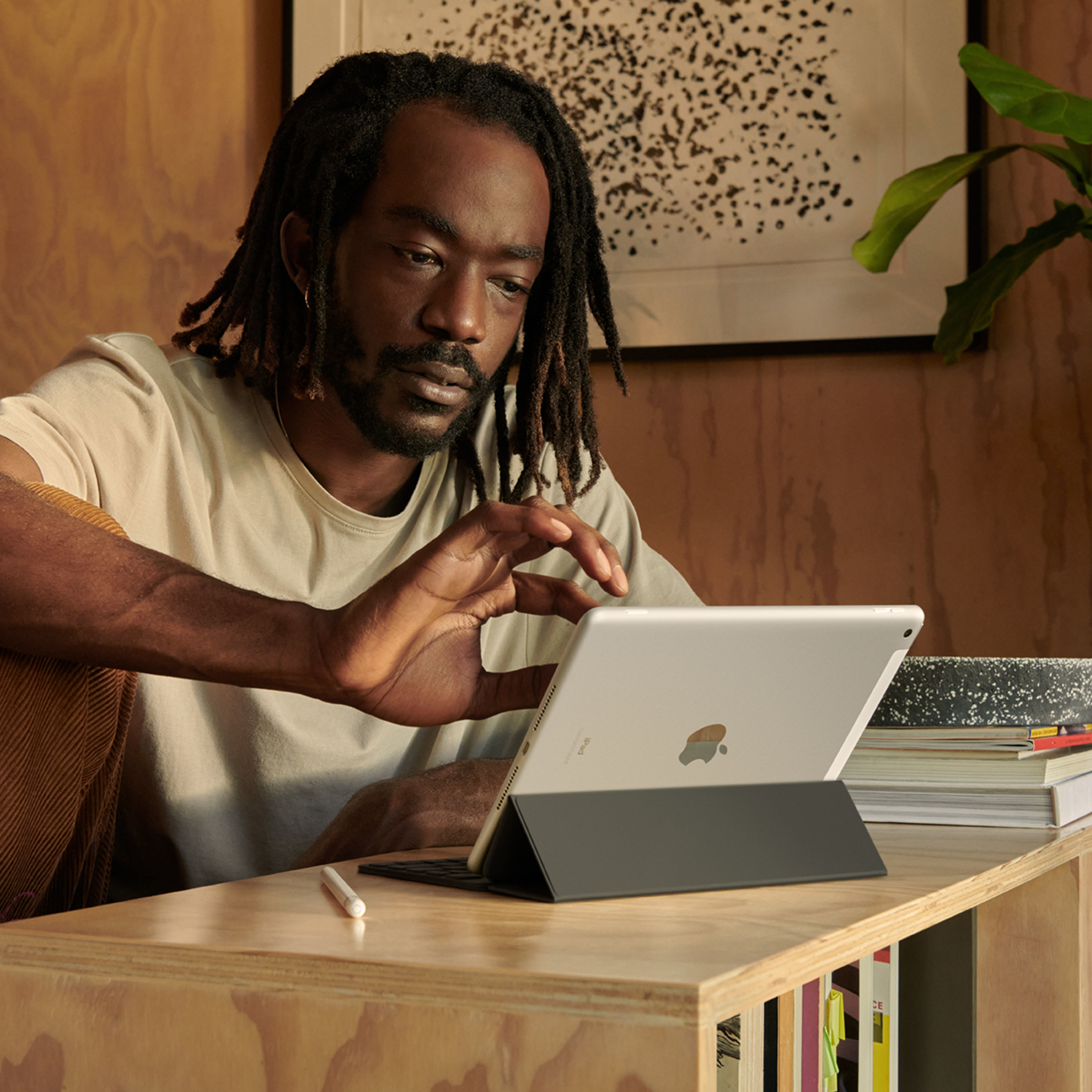 Mężczyzna z dredami używający tabletu z klawiaturą na drewnianym biurku. Ujęcie wnętrza.