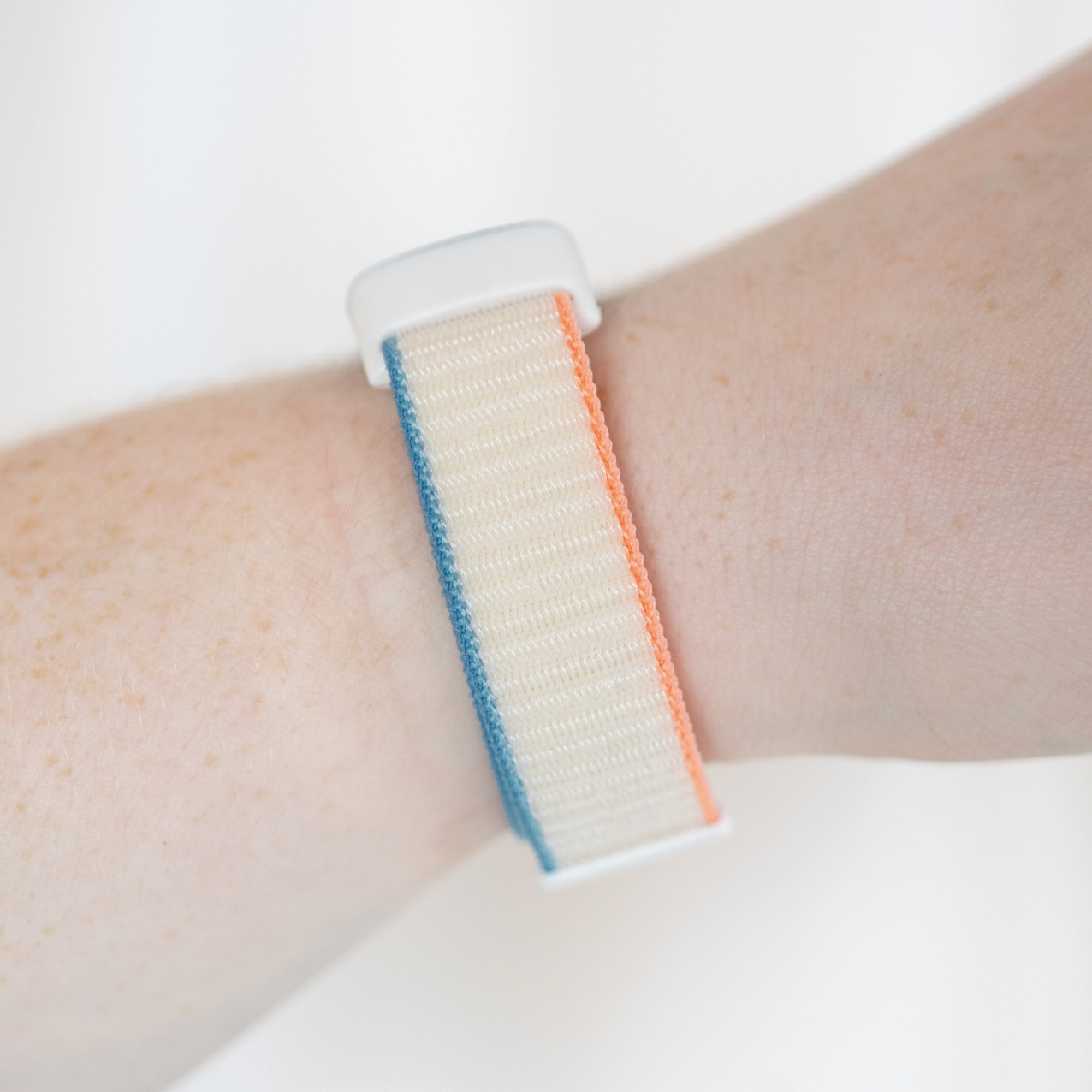 Handgelenk mit Armbanduhr. Das Band ist beige mit blauen und orangefarbenen Streifen.
