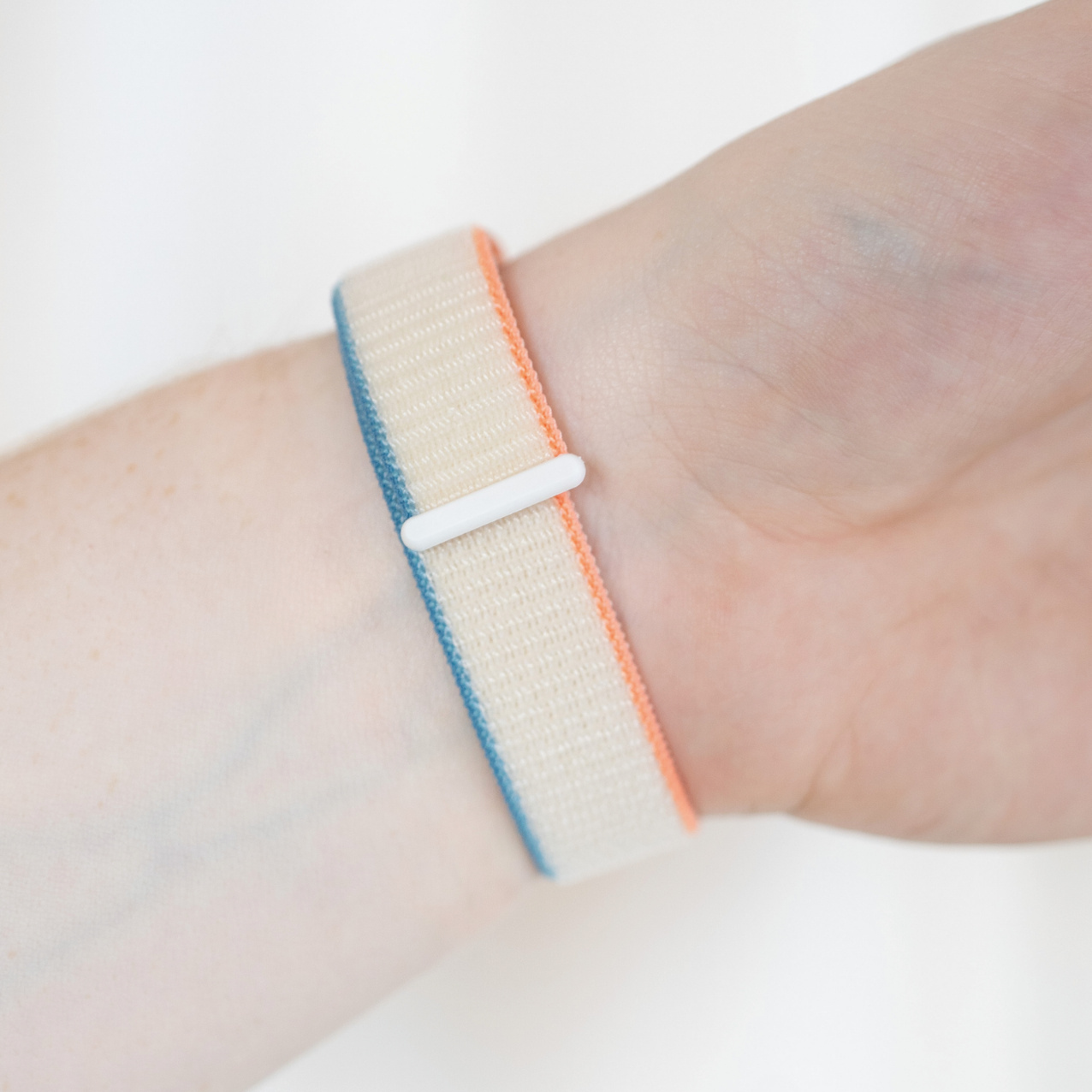 Ein Handgelenk mit einem mehrfarbigen Armband. Es hat orange, blaue und beige Farben.