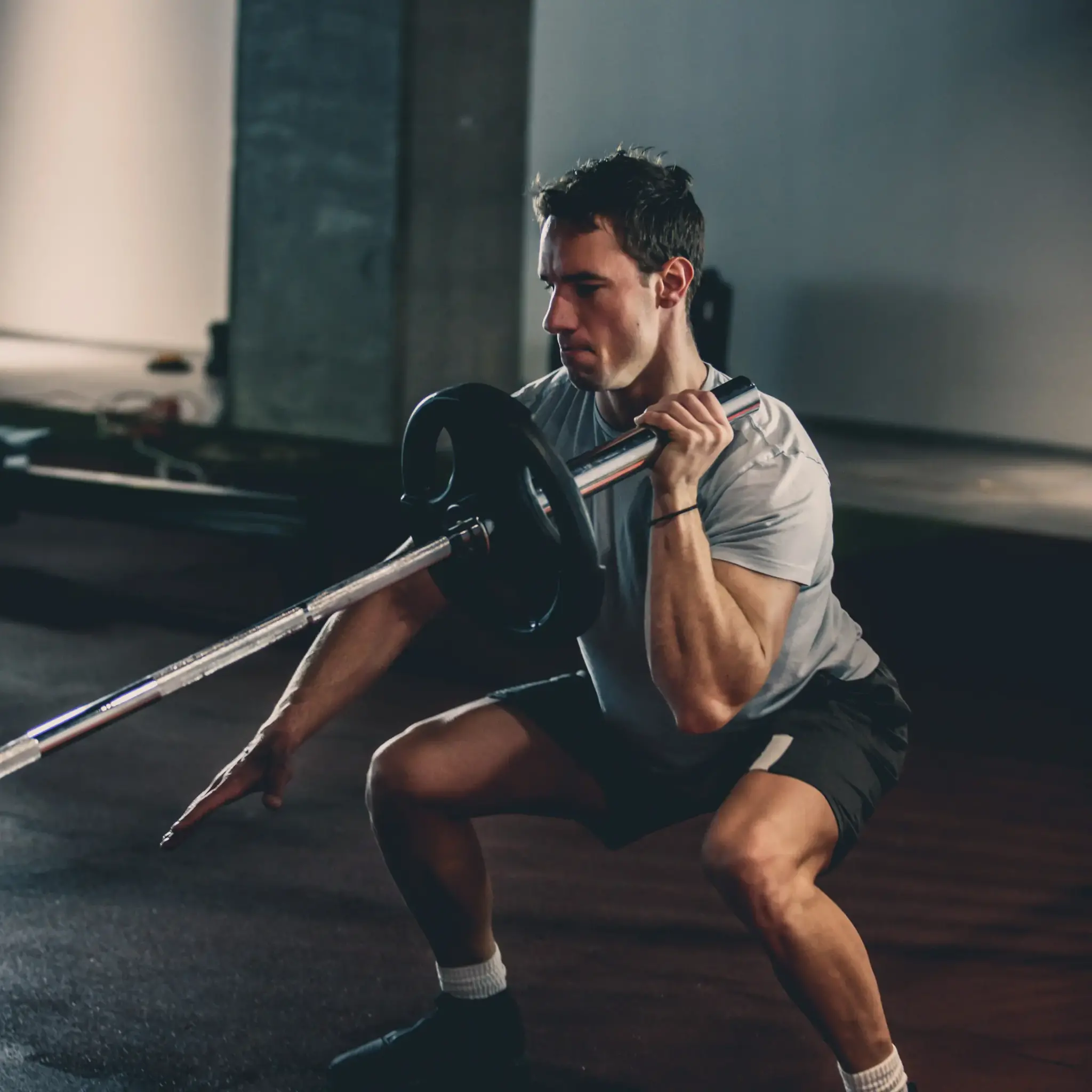 A man is in a gym, lifting a barbell while doing squats. Focus is on the action, training.