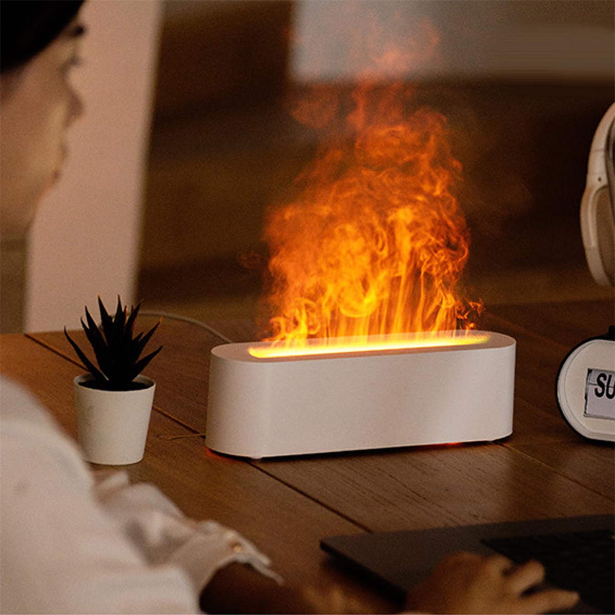 Ein weißer Flammen-Luftbefeuchter auf einem Holztisch mit einer Person im Hintergrund.
