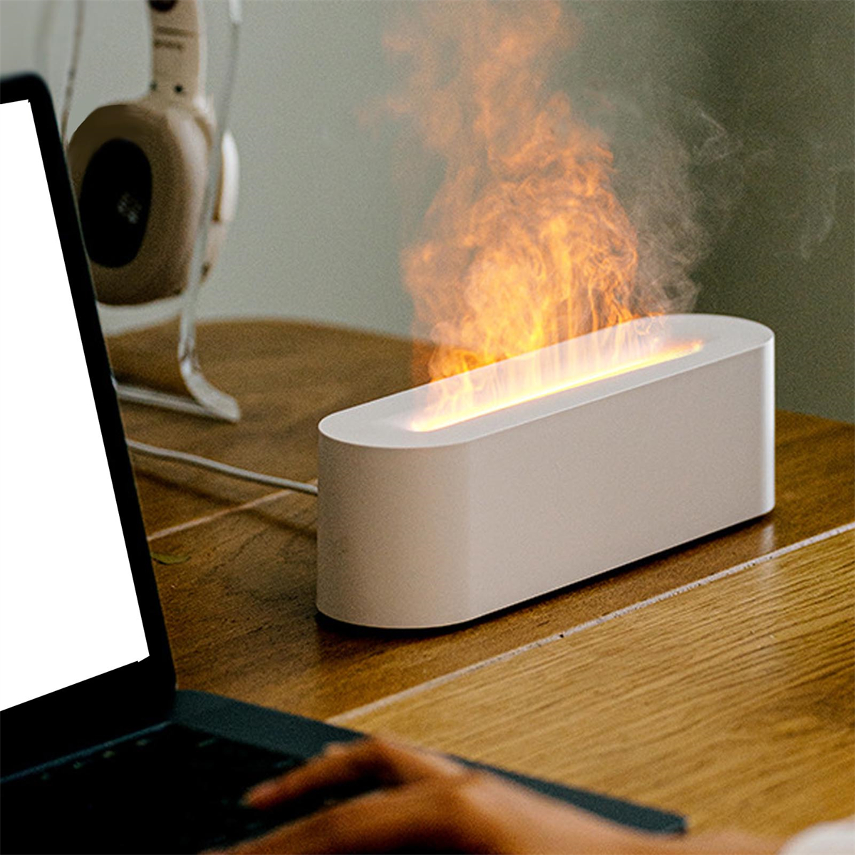 Weißer, flammensimulierender Luftbefeuchter. Laptop und Kopfhörer im Hintergrund. Holztisch.