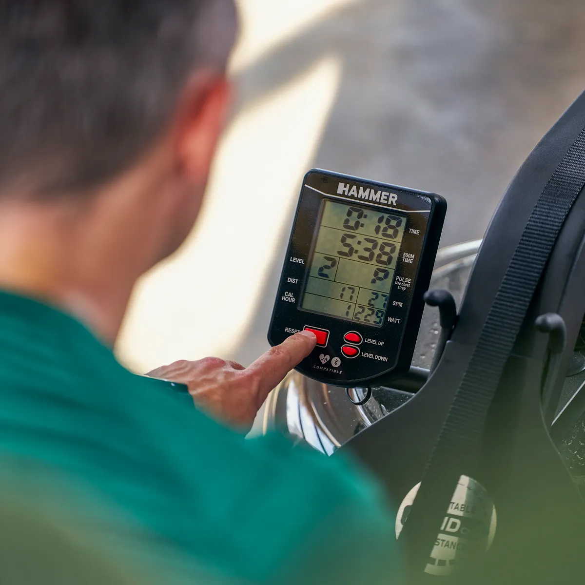 Ein Mann berührt eine digitale Anzeige auf einem Heimtrainer. Die Anzeige zeigt Zeit, Entfernung und Geschwindigkeit.