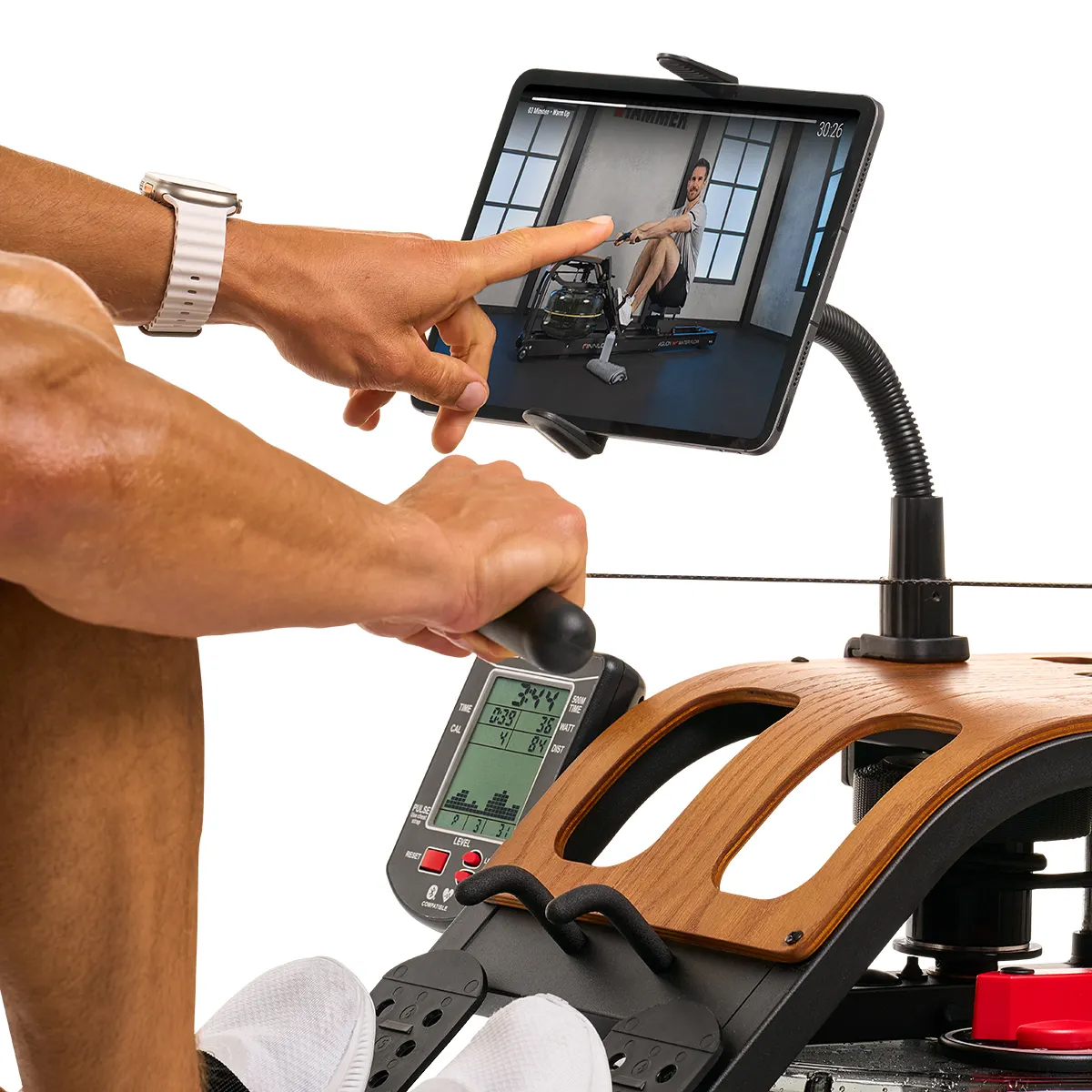 Ein Mann benutzt ein Rudergerät. Ein Tablet zeigt ein Trainingsvideo und die Anzeige des Geräts zeigt Statistiken.