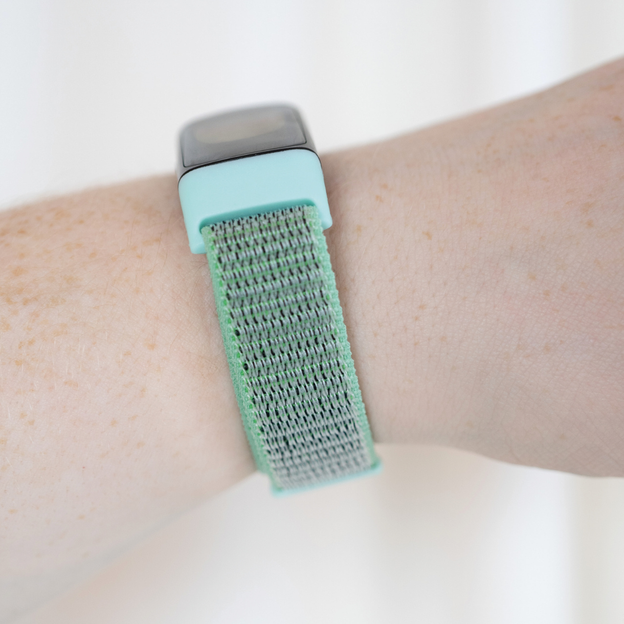 Ein Handgelenk mit einem mintgrünen und grauen Stoff-Smartband wird im Nahaufnahme gezeigt.