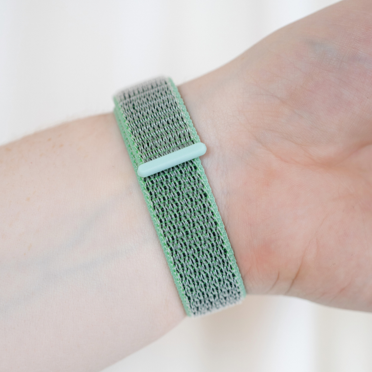 Ein Handgelenk mit einem grünen und grauen Stoff-Uhrenarmband, gesichert durch eine hellgrüne Schließe.
