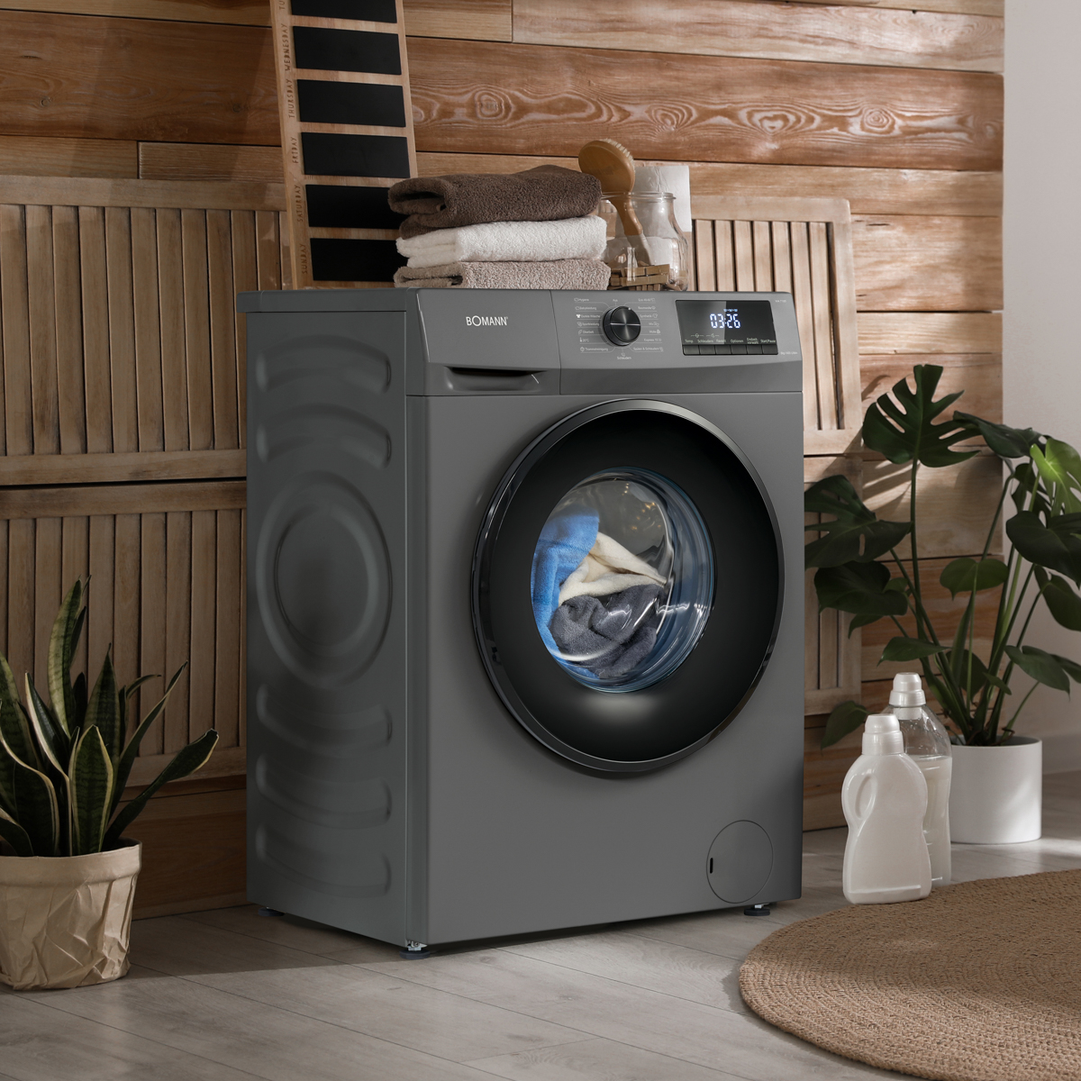 Eine graue Waschmaschine mit Glastür in einem Raum mit Pflanzen und Holzpaneelen.