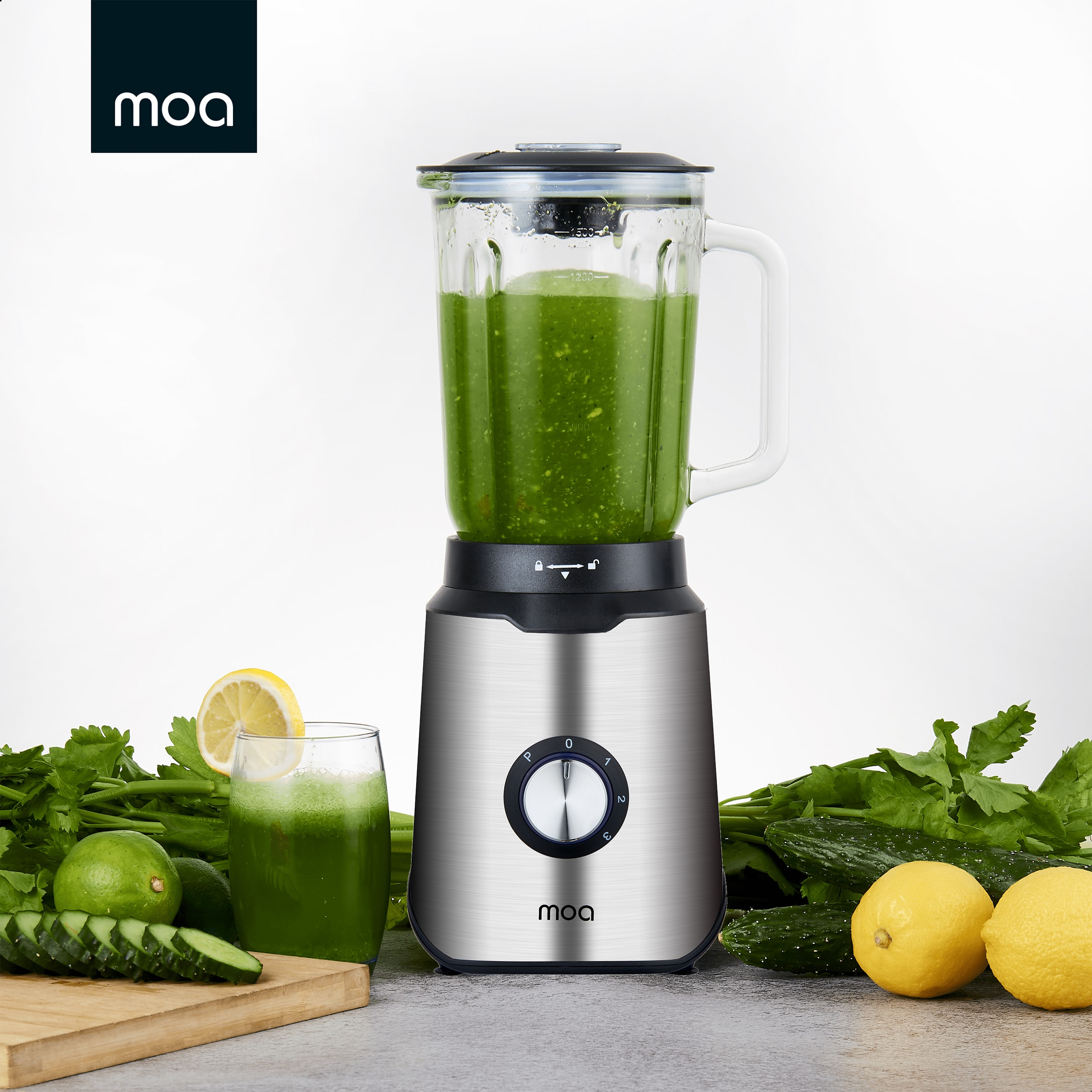 Blender with green liquid, glass with drink, lemons, and cucumber on a table.