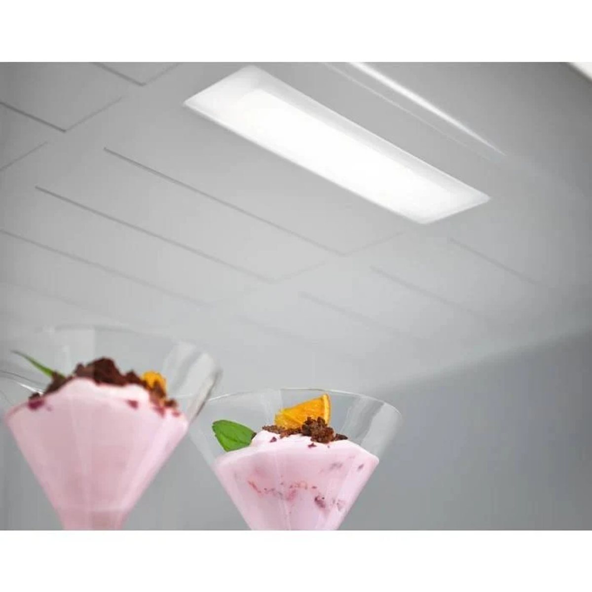 Twee dessertglazen met roze crème en sinaasappel. Gereflecteerd licht op een wit oppervlak.