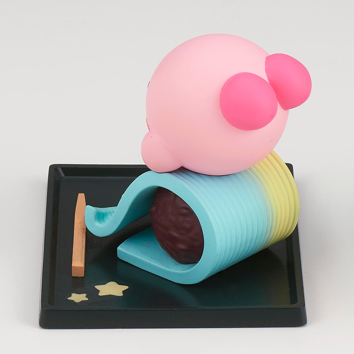 Rosa Kirby-Figur auf einem schwarzen Tablett mit einem braunen Stock und zwei goldenen Sternen.