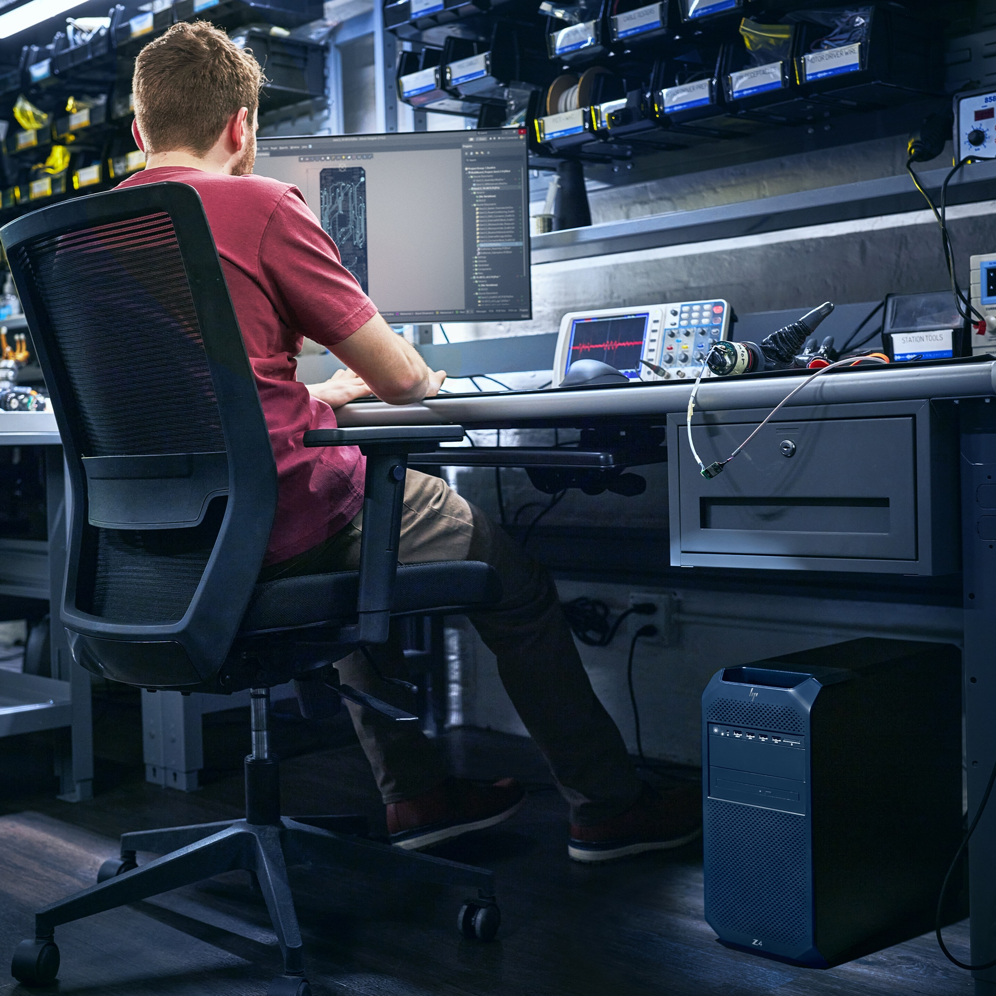 Mężczyzna pracujący na komputerze w laboratorium technologicznym. Siedzi, patrząc na ekran, z wyposażeniem laboratoryjnym w tle.