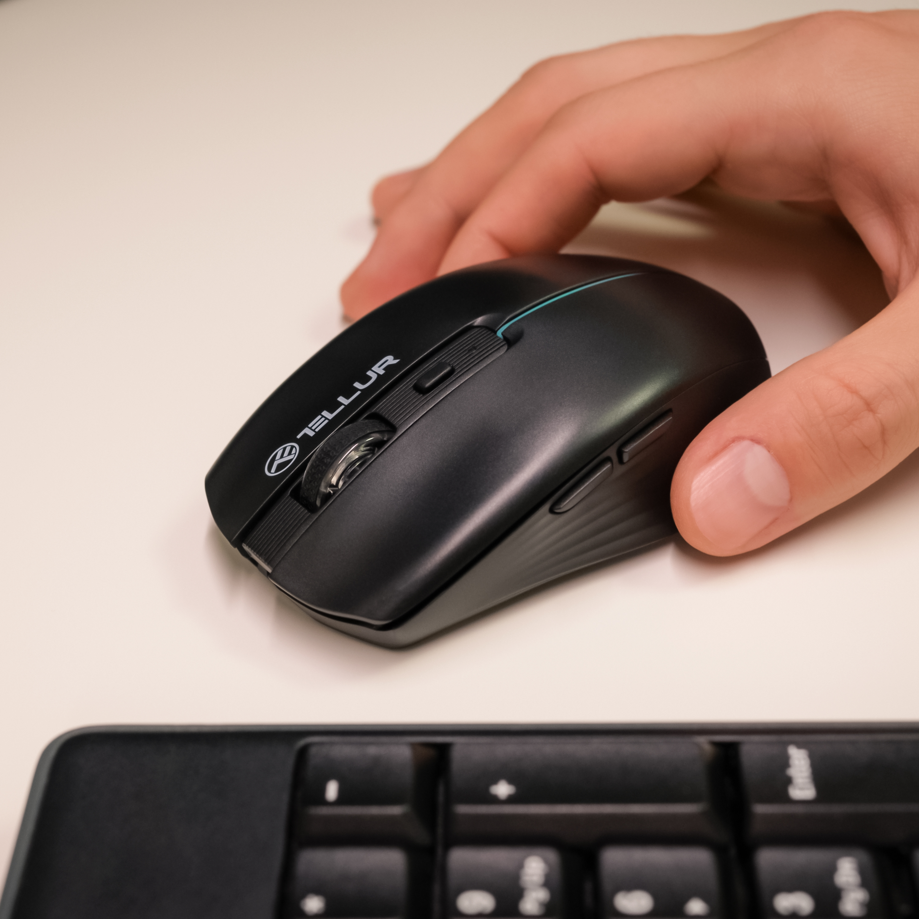 Ręka osoby dotykająca czarnej myszy bezprzewodowej na białym biurku z klawiaturą.