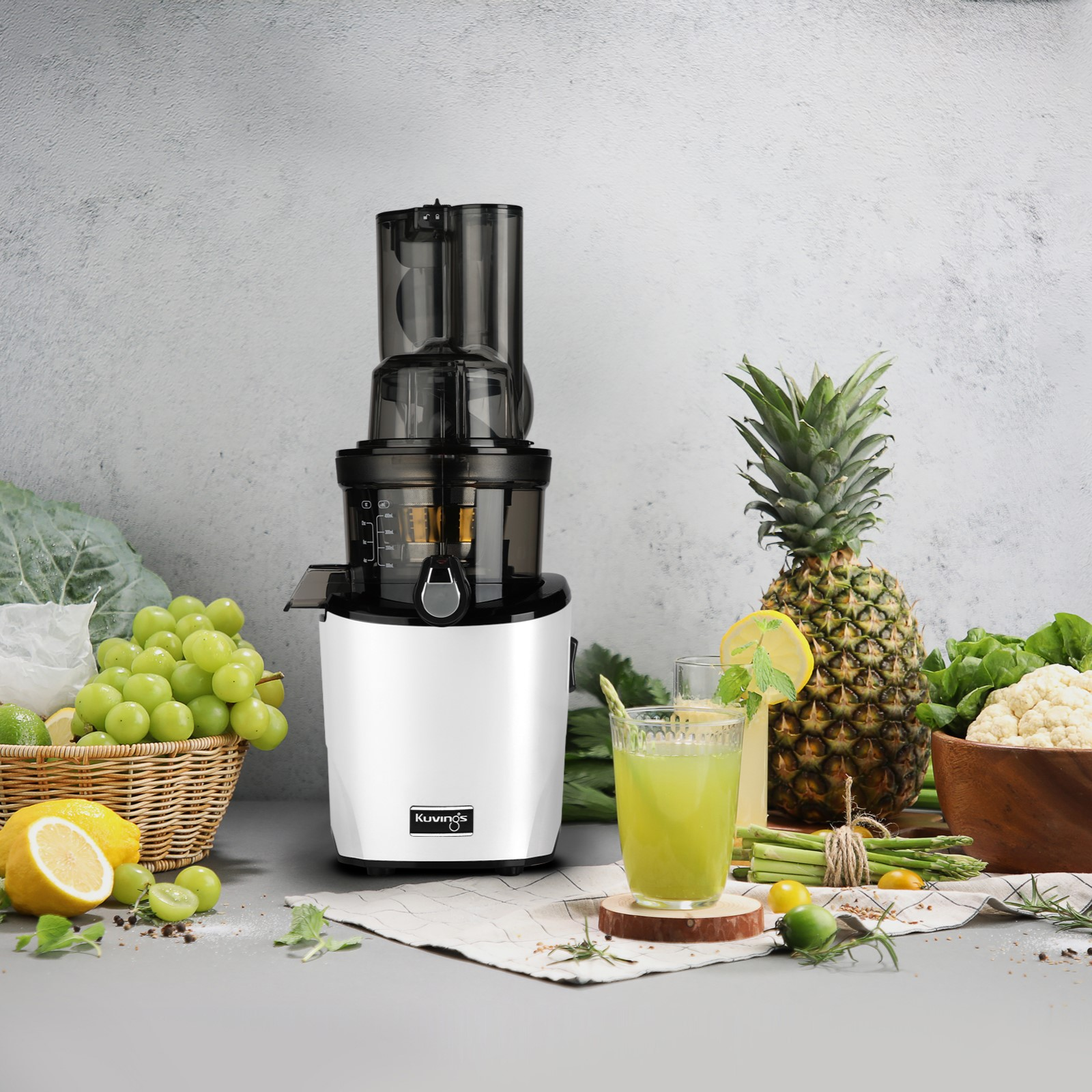 Centrifuga, frutta e bicchiere di succo sul tavolo. Ananas e altra frutta sullo sfondo.