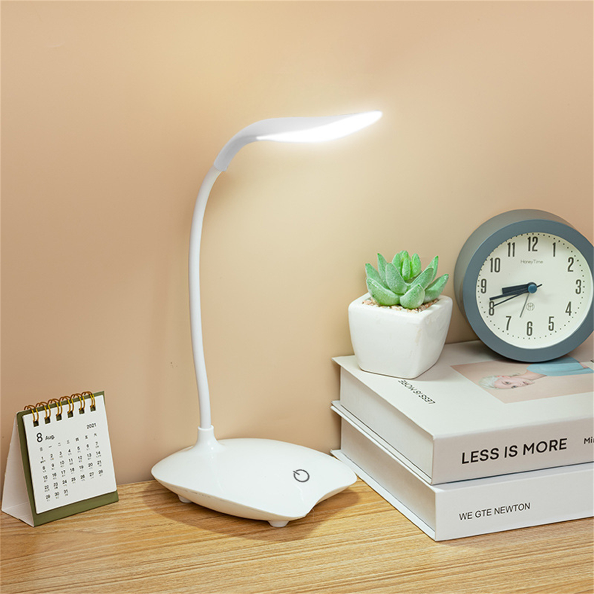 Schreibtischlampe, Uhr, Kalender, Bücher und eine kleine Pflanze auf Holzoberfläche. Beiger Hintergrund.