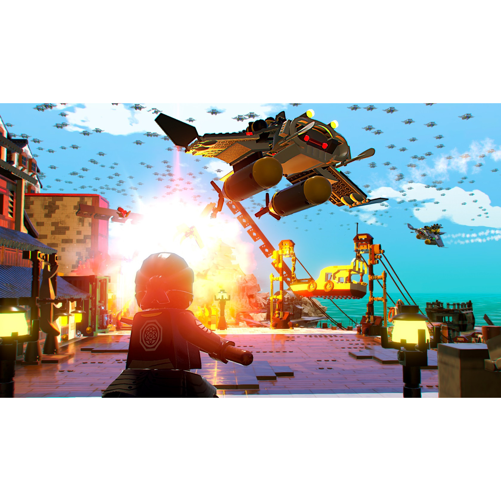 Scena del gioco Lego Ninjago. Un personaggio punta un'arma contro un veicolo volante. Edifici in fiamme sullo sfondo.