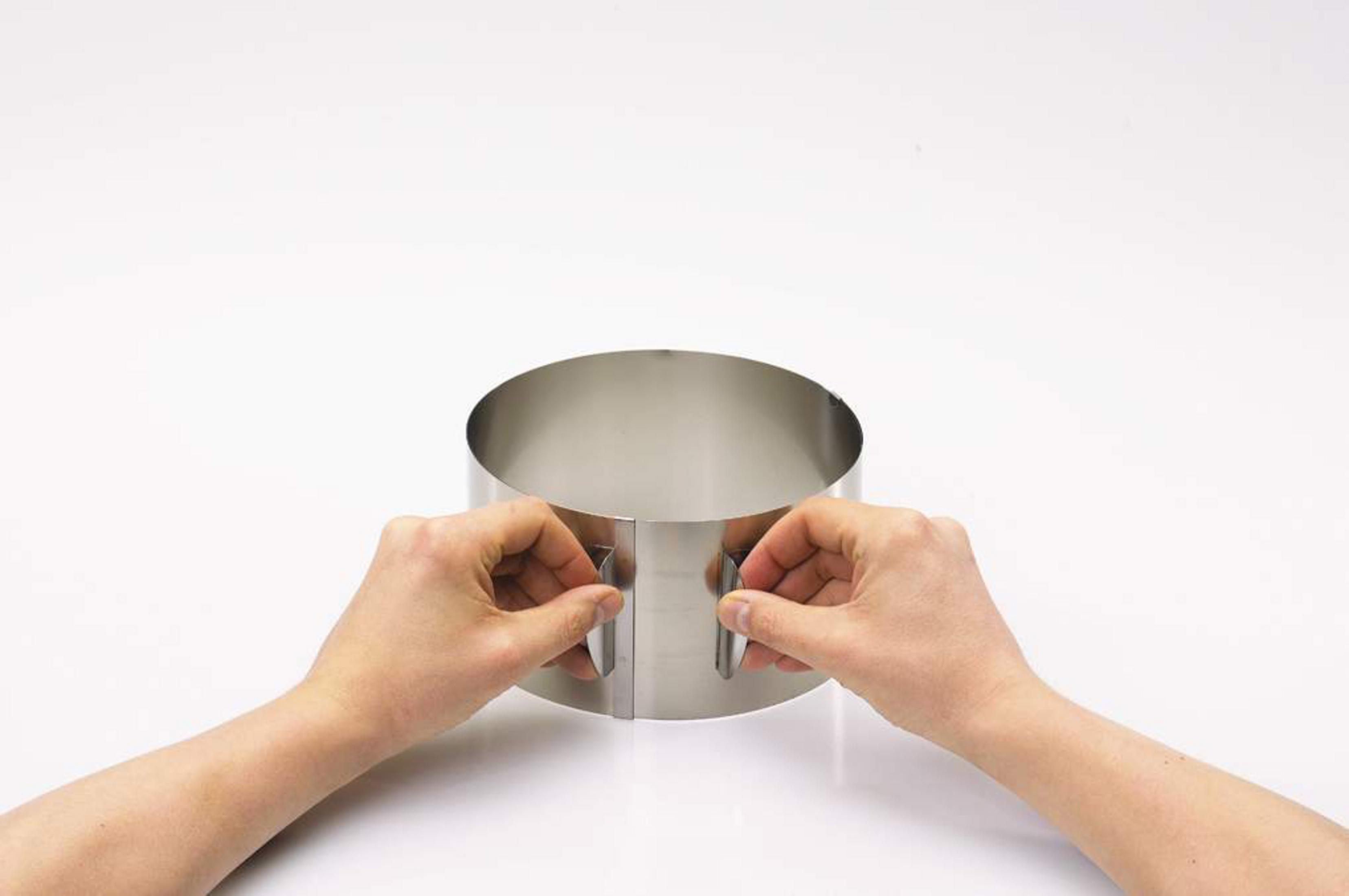 Mains tenant et ajustant un cercle à gâteau en acier inoxydable sur fond blanc.