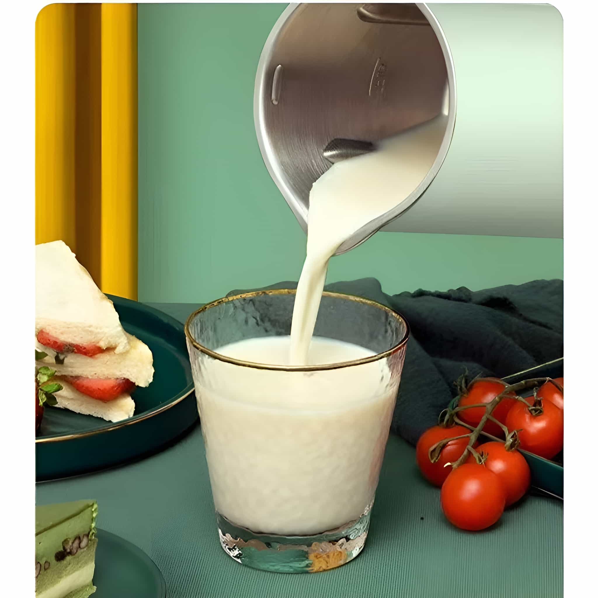 Milch wird in ein Glas gegossen, daneben Sandwiches und Tomaten auf grünem Tisch.