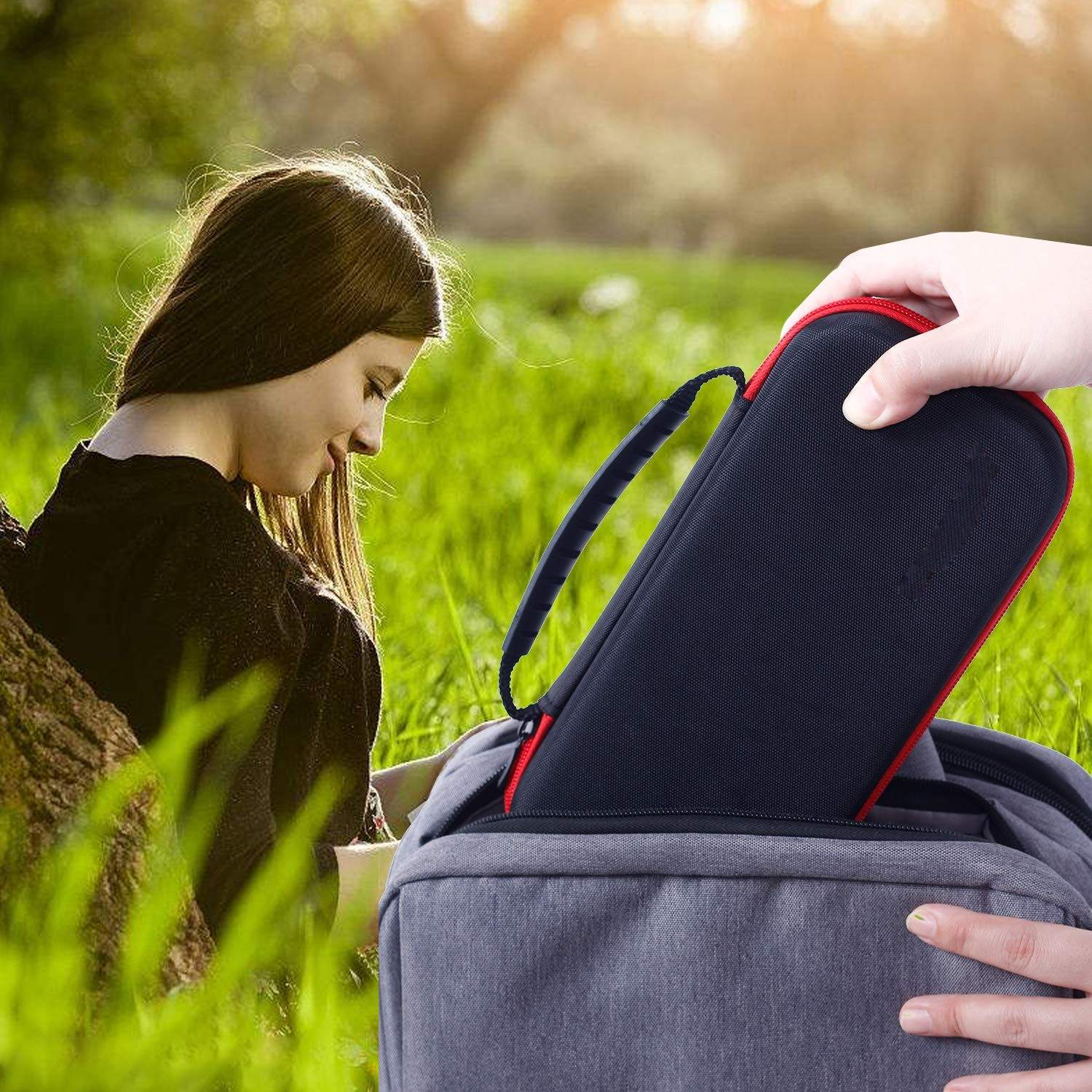 Frau, die einen schwarzen Koffer mit rotem Rand in einen grauen Rucksack packt, im Freien.
