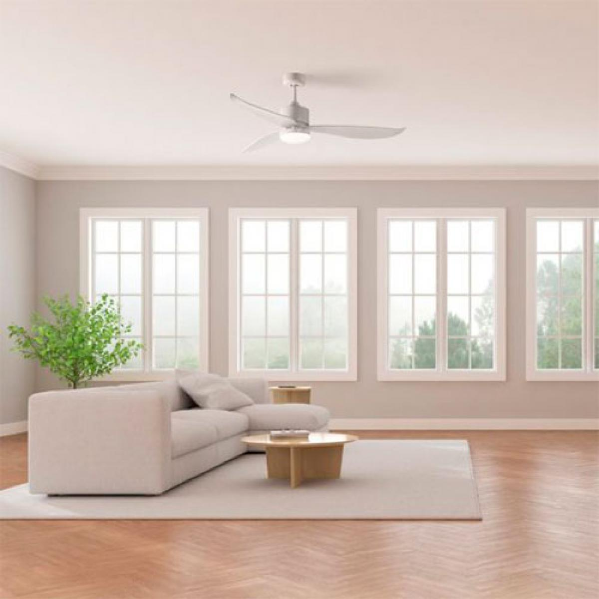 Wnętrze salonu z białą sofą, drewnianą podłogą i wentylatorem sufitowym. Okna z widokiem na zewnątrz.
