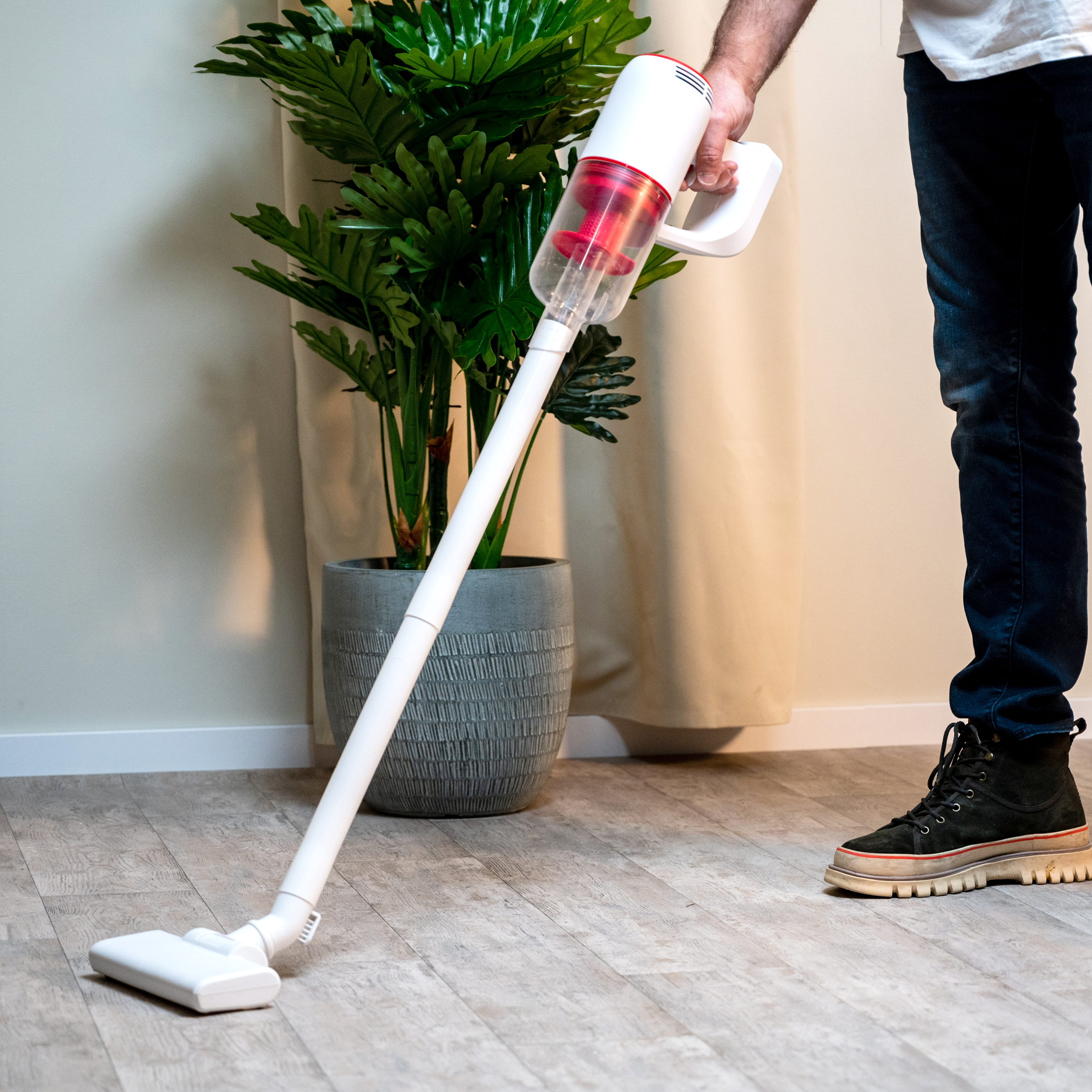 Personne passe l'aspirateur sur un plancher en bois avec un aspirateur blanc et rouge. Une plante en arrière-plan.