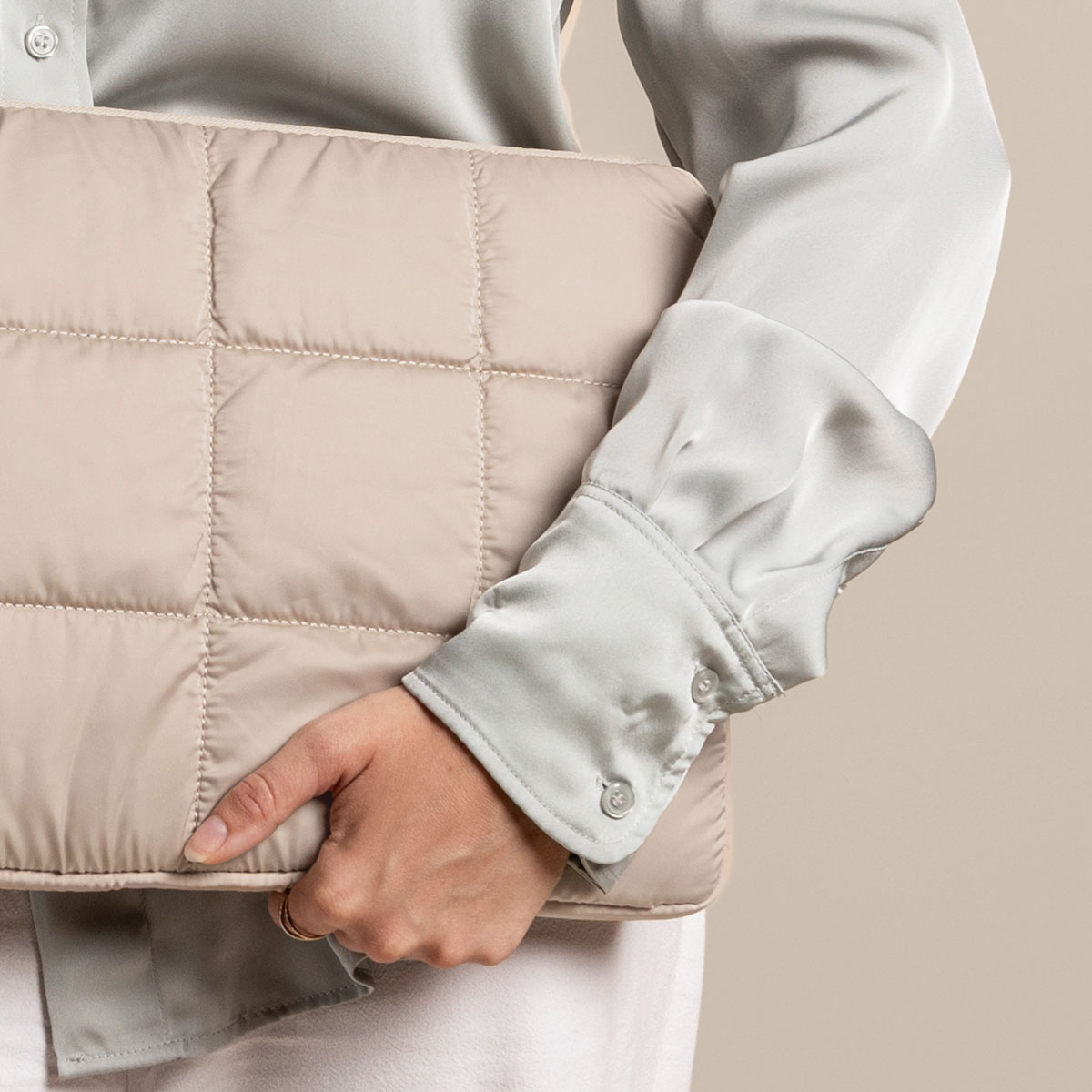 Person holding a beige, quilted laptop case, wearing a light green shirt and white pants.
