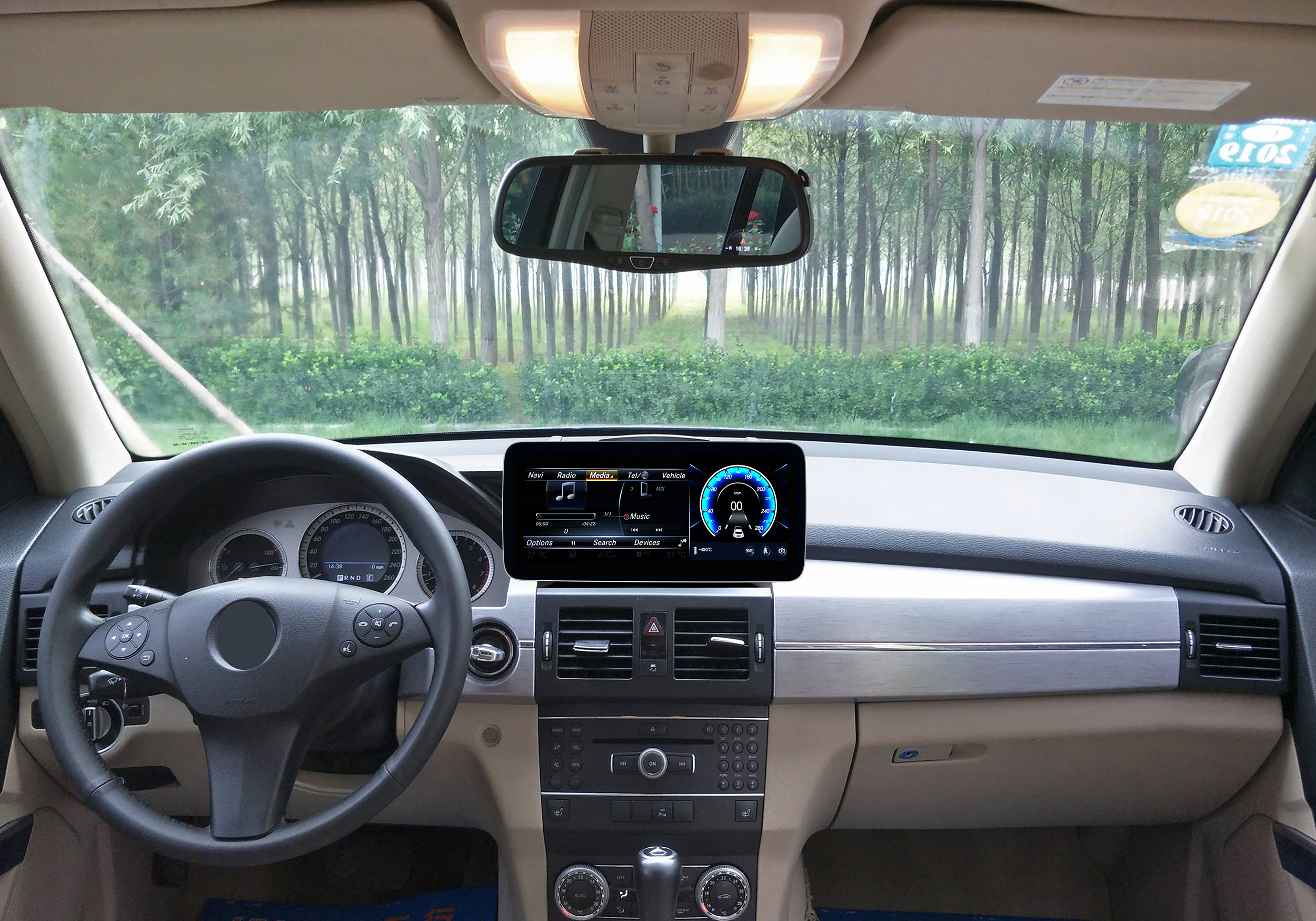 Innenansicht eines Autos mit Armaturenbrett, Display, Lenkrad und Baumhintergrund.