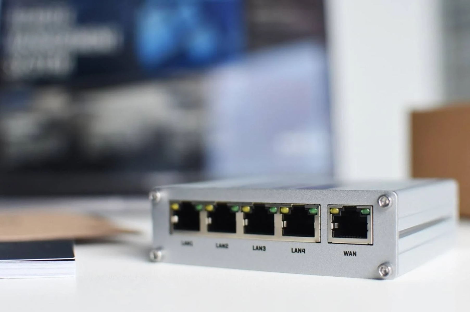 Router argentato con porte LAN e WAN. Superficie bianca, sfondo sfocato.