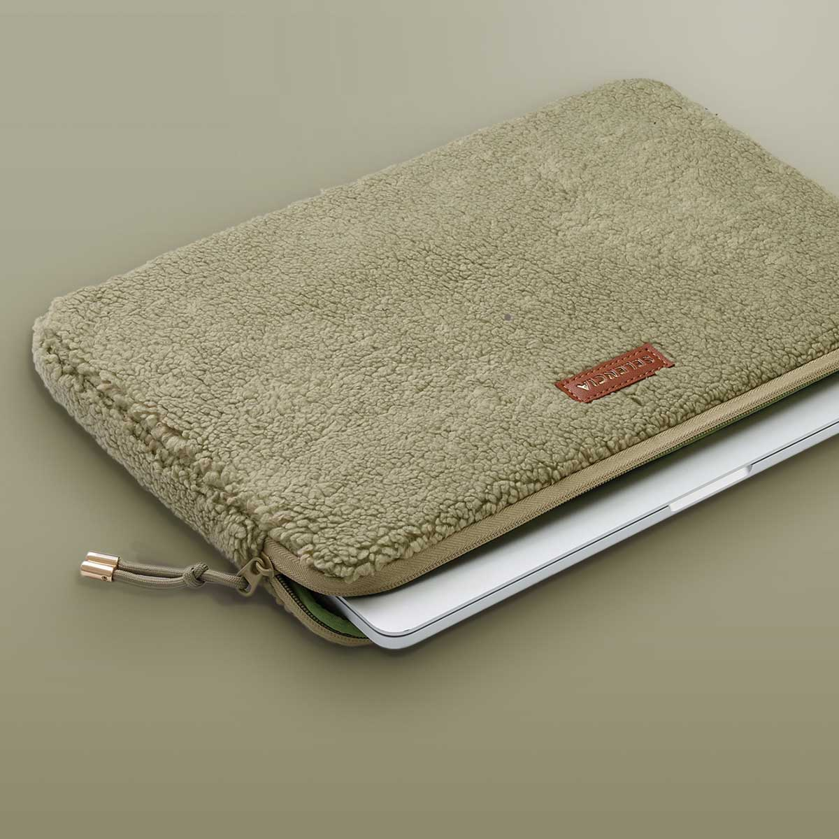 Laptop in a fluffy olive-green case. Brown label says 'YOLICA'. Zipper and gold-tone pull.