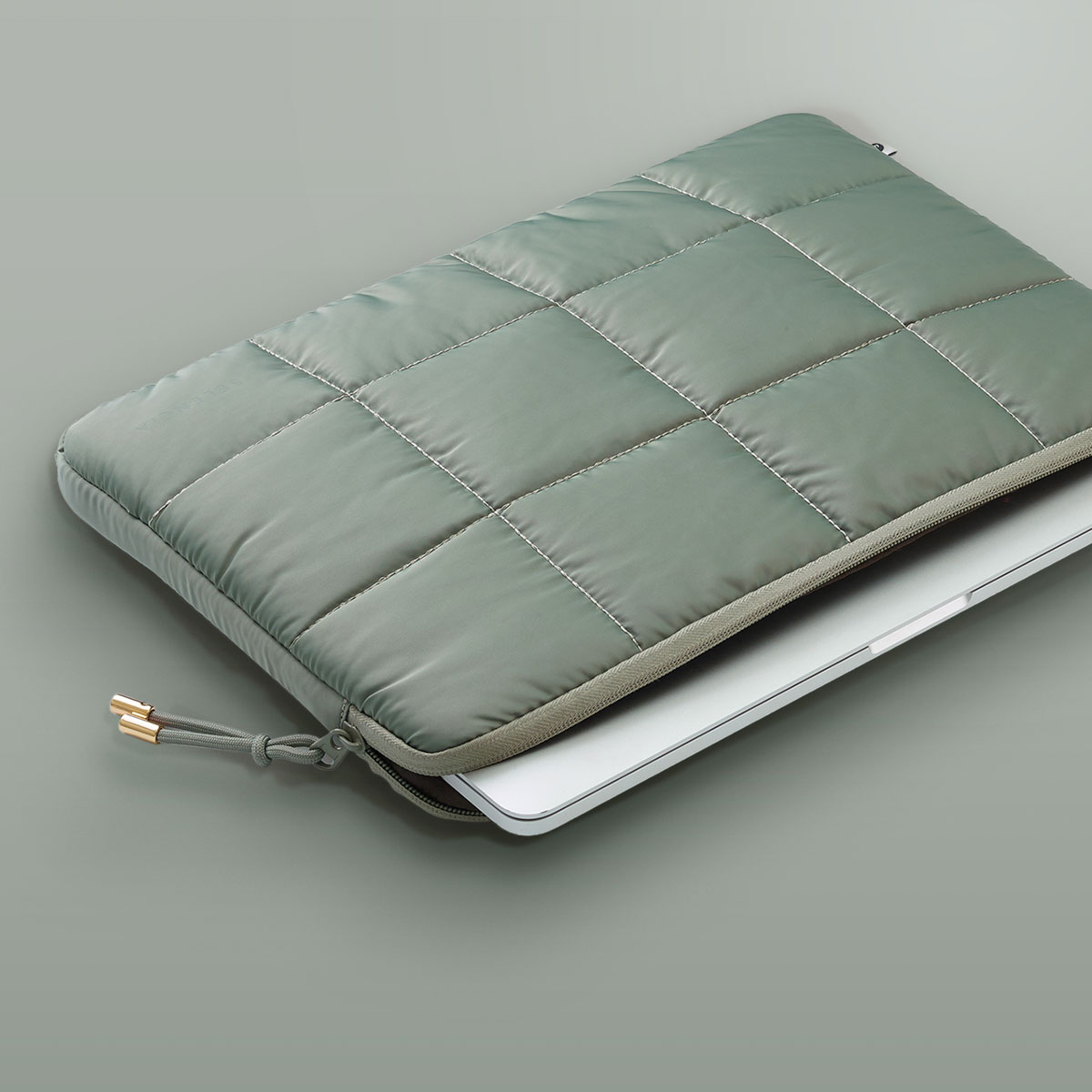 Green quilted laptop sleeve with a zipper and gold accents.