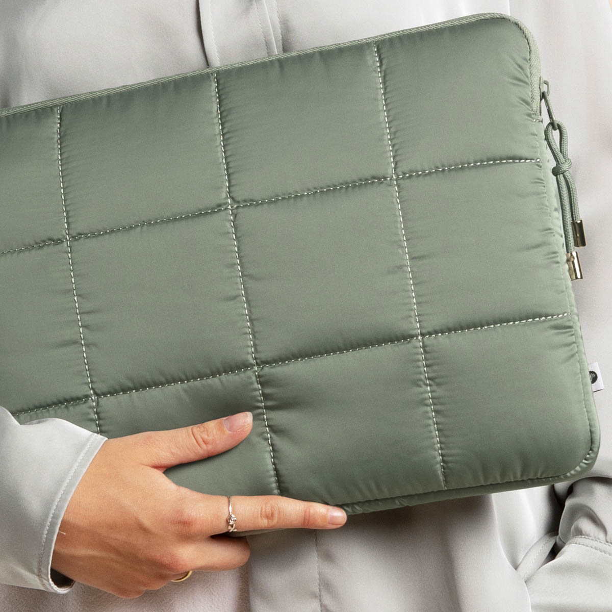 Laptop sleeve, quilted, olive green. Person holding it. Neutral background.