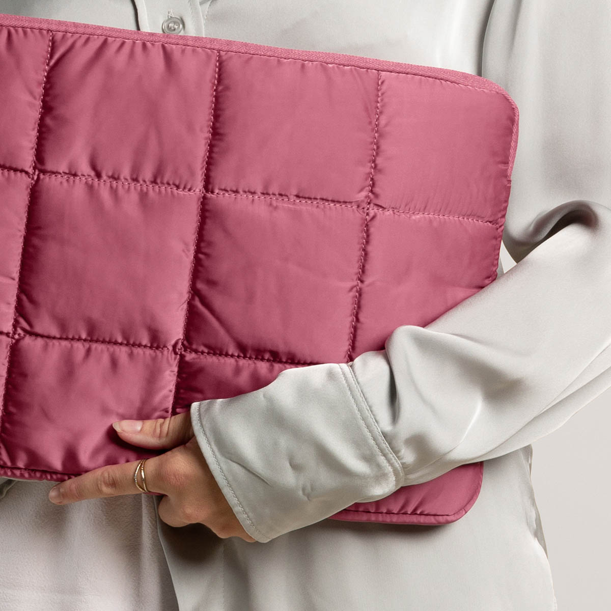 Person points to a pink, quilted laptop sleeve. The sleeve is on a light background.