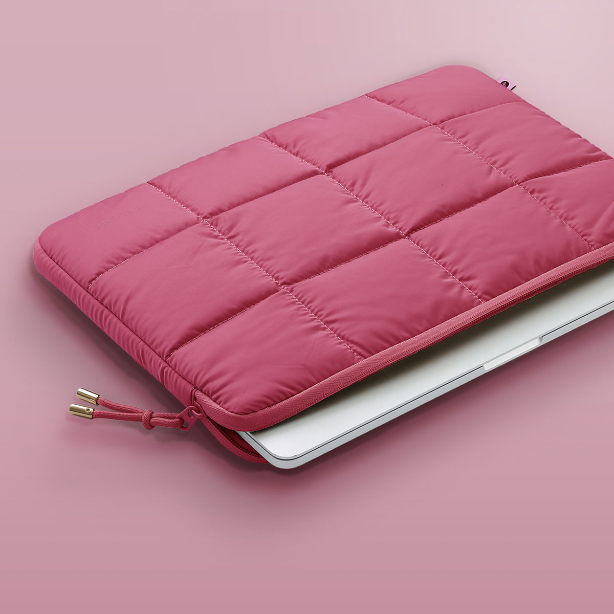 A pink quilted laptop sleeve with a silver zipper, partially open, revealing a laptop inside.