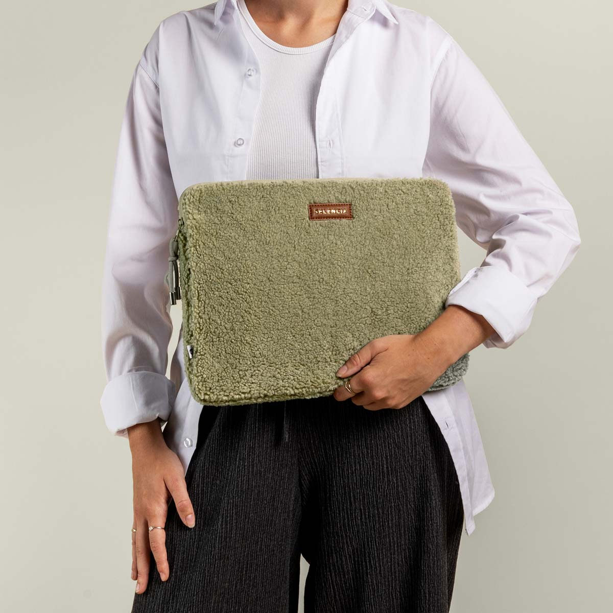 Woman holding a green fuzzy laptop sleeve. She wears a white shirt and dark pants.