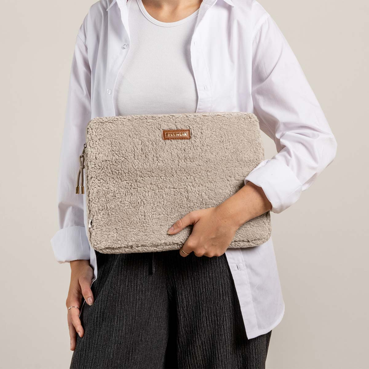 Woman holding a fluffy beige laptop sleeve with a brown label.