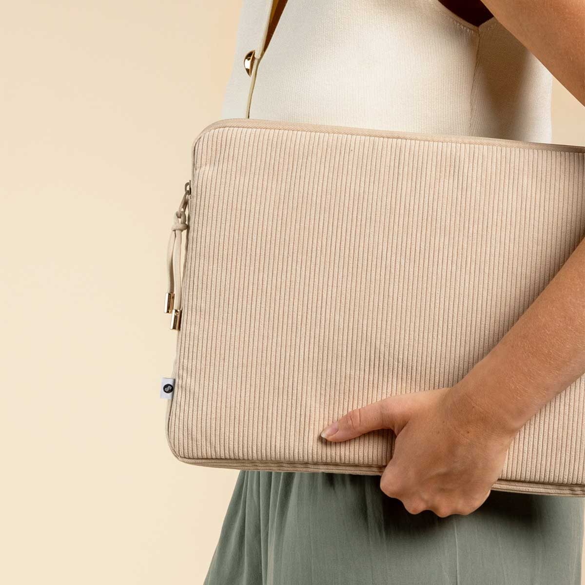 A woman holding a beige corduroy laptop sleeve. The sleeve is beige and has a zipper.