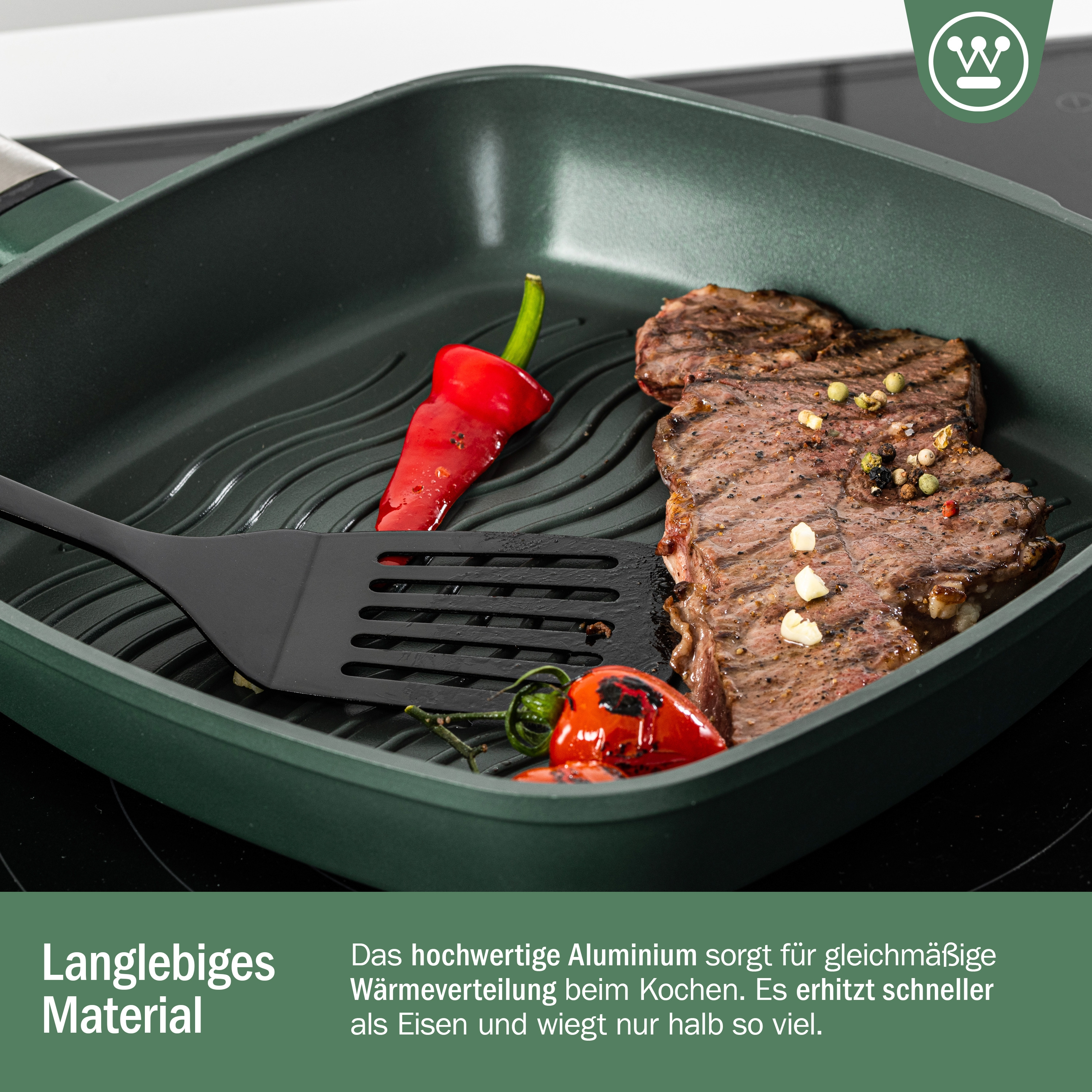 Grüne Bratpfanne mit Steak, roter Paprika und Pfannenwender auf Herdplatte.