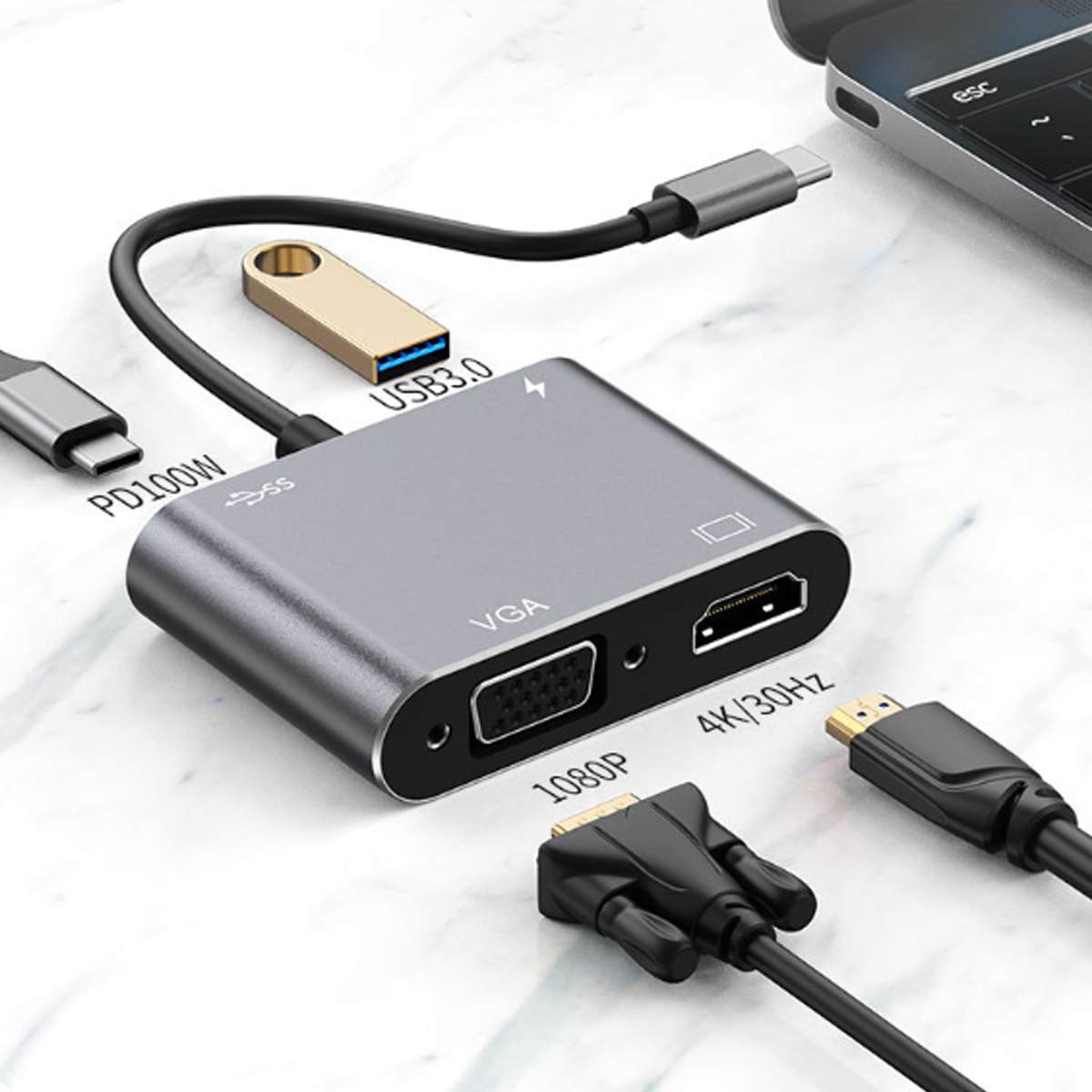 Ein grauer USB-C-Hub mit VGA- und HDMI-Anschlüssen, angeschlossenen Kabeln und einem goldenen USB-Laufwerk. Im Hintergrund ein Laptop.