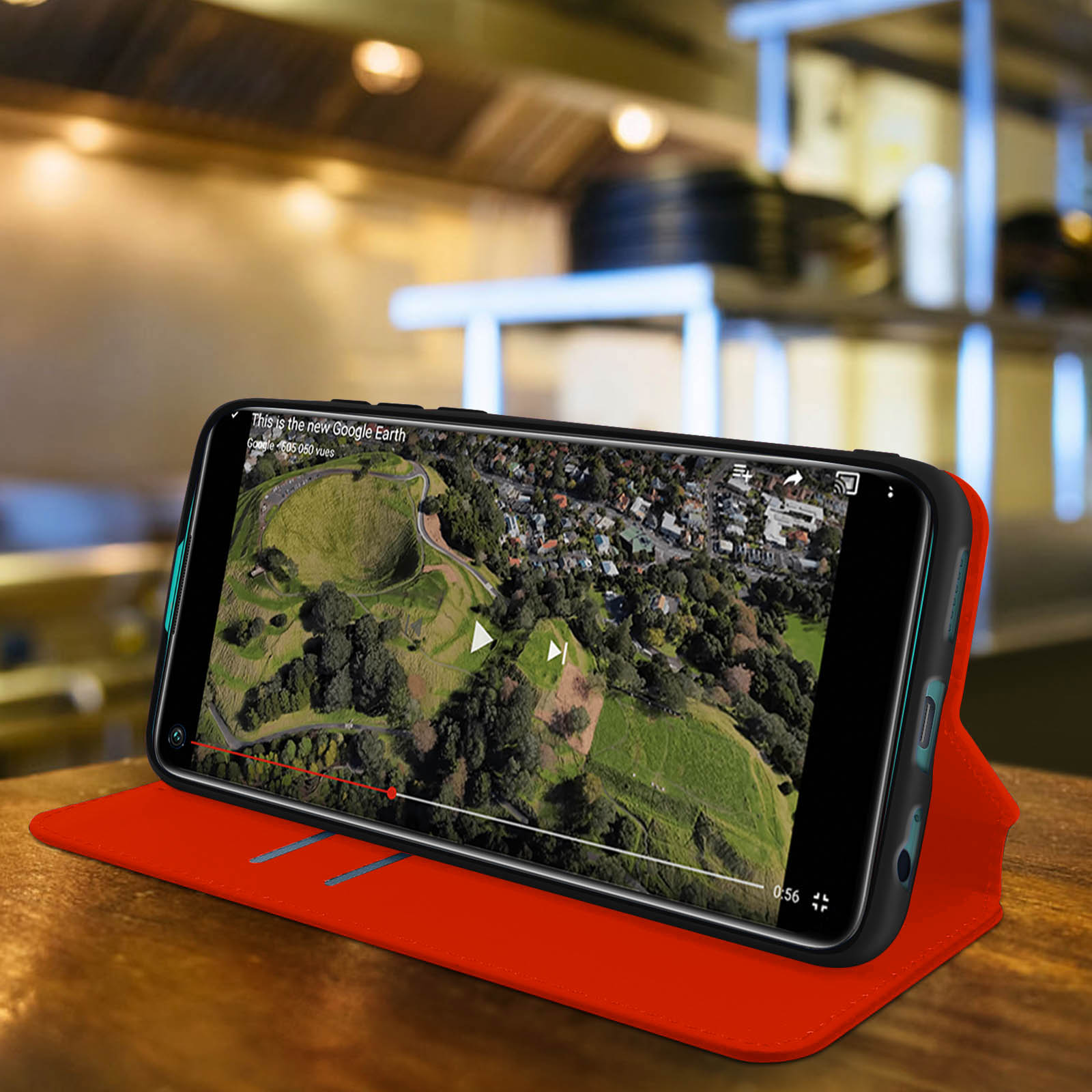 Een telefoon in een rode hoes toont een video van een landschap op een houten tafel.