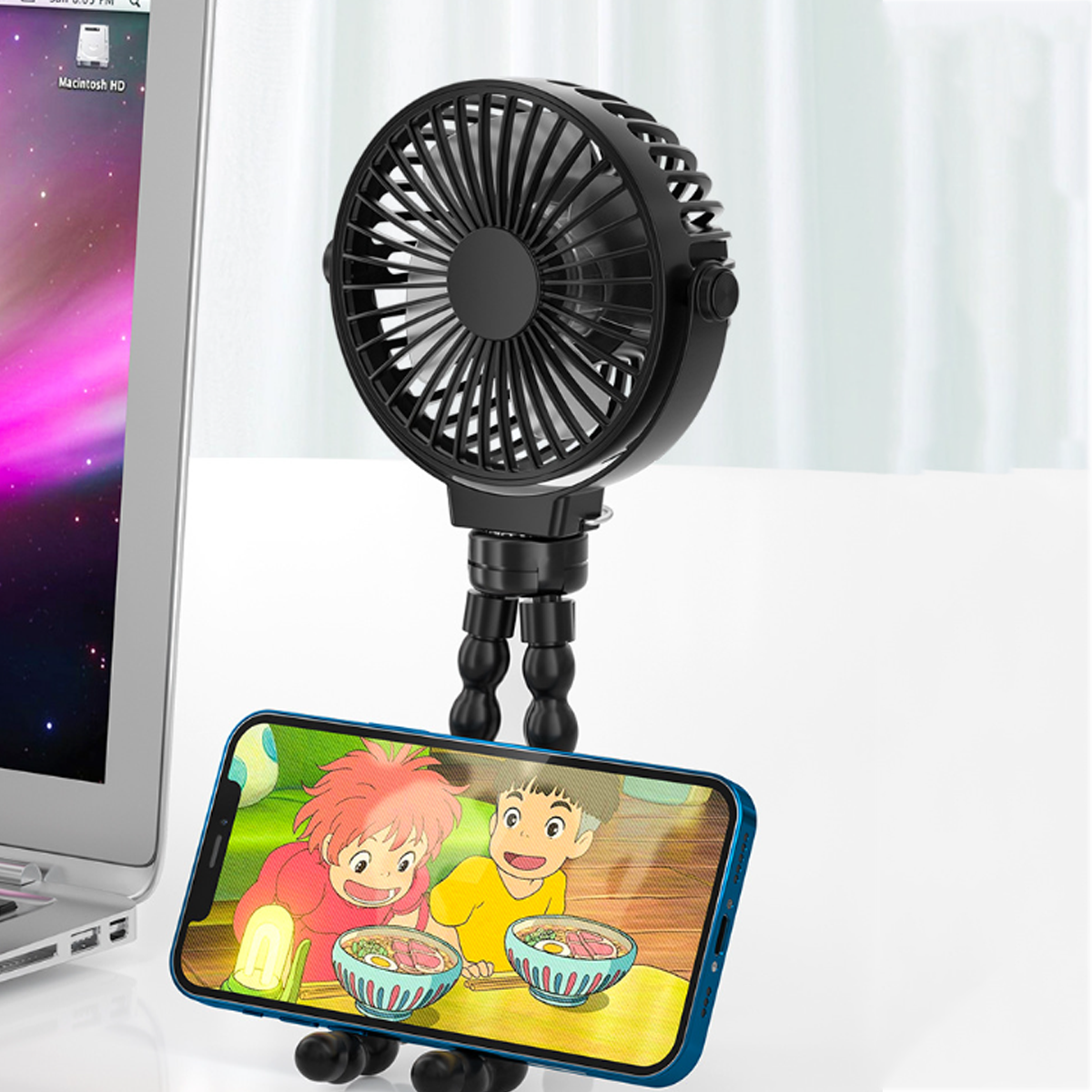Mini-Ventilator auf flexiblen Beinen, der ein Telefon hält, das animierte Charaktere auf dem Bildschirm zeigt. Laptop im Hintergrund.