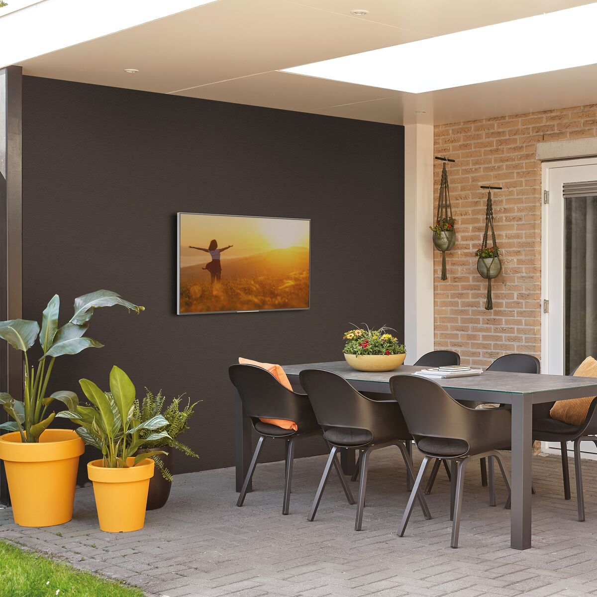 Outdoor-Terrassenbereich mit einem an der Wand montierten Fernseher, Stühlen und Pflanzen.