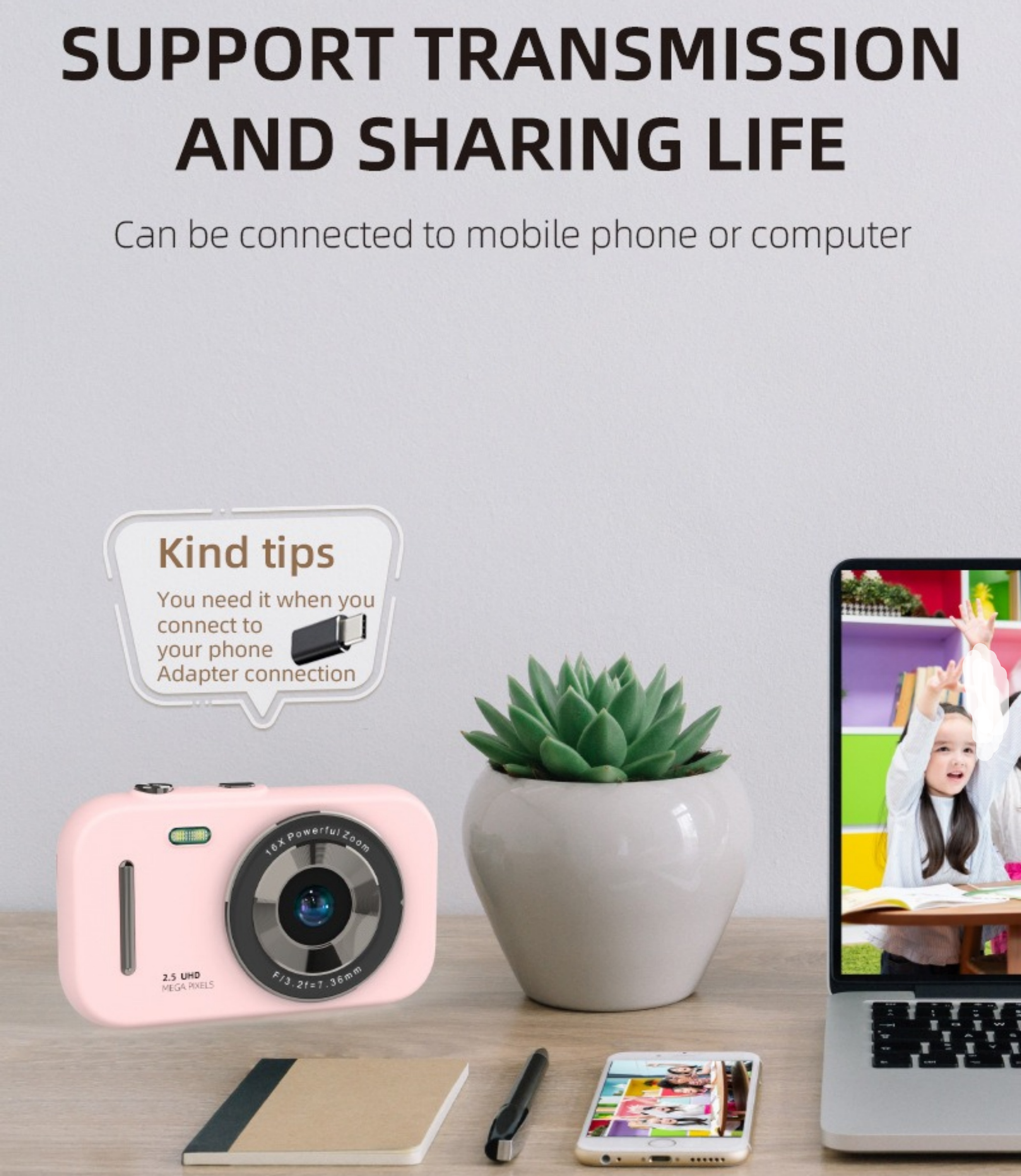 Eine rosa Kamera, eine grüne Pflanze, ein Laptop und ein Telefon liegen auf einem Holztisch. Der Hintergrund ist verschwommen.