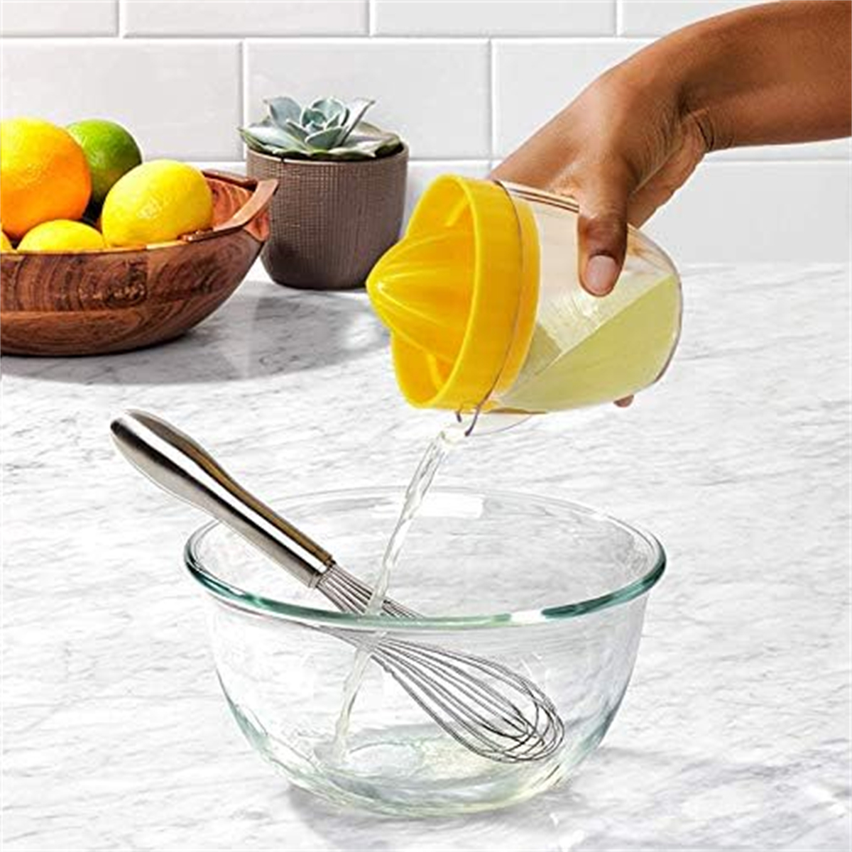 Person, die Zitronensaft in eine Glasschüssel presst, Schneebesen und Zitronen im Hintergrund.