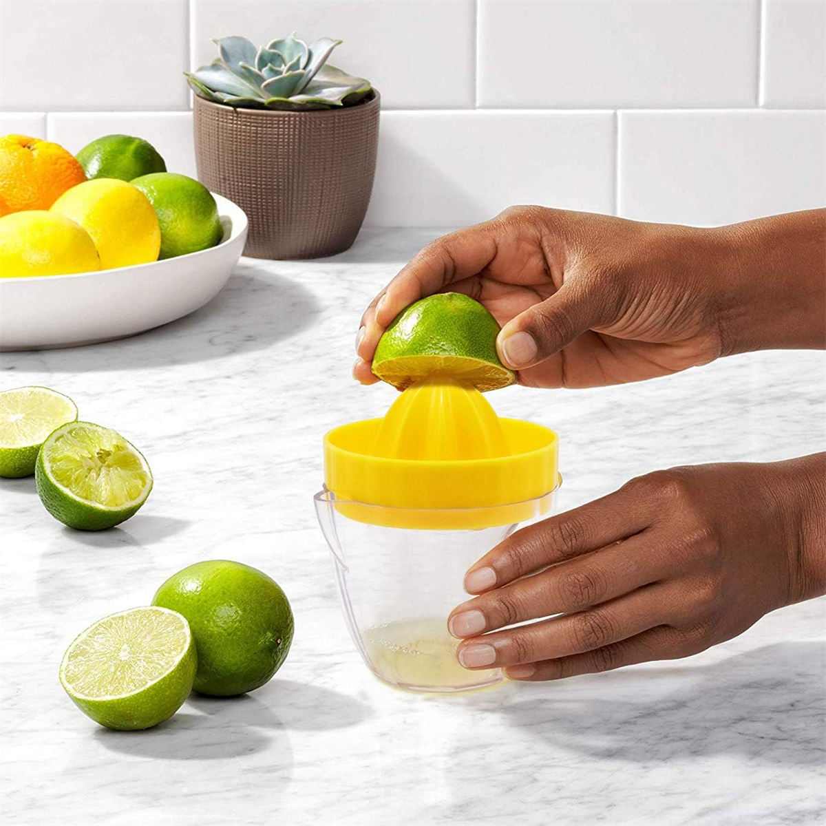 Person presst eine Limettenhälfte in eine gelbe Saftpresse über einem durchsichtigen Behälter.