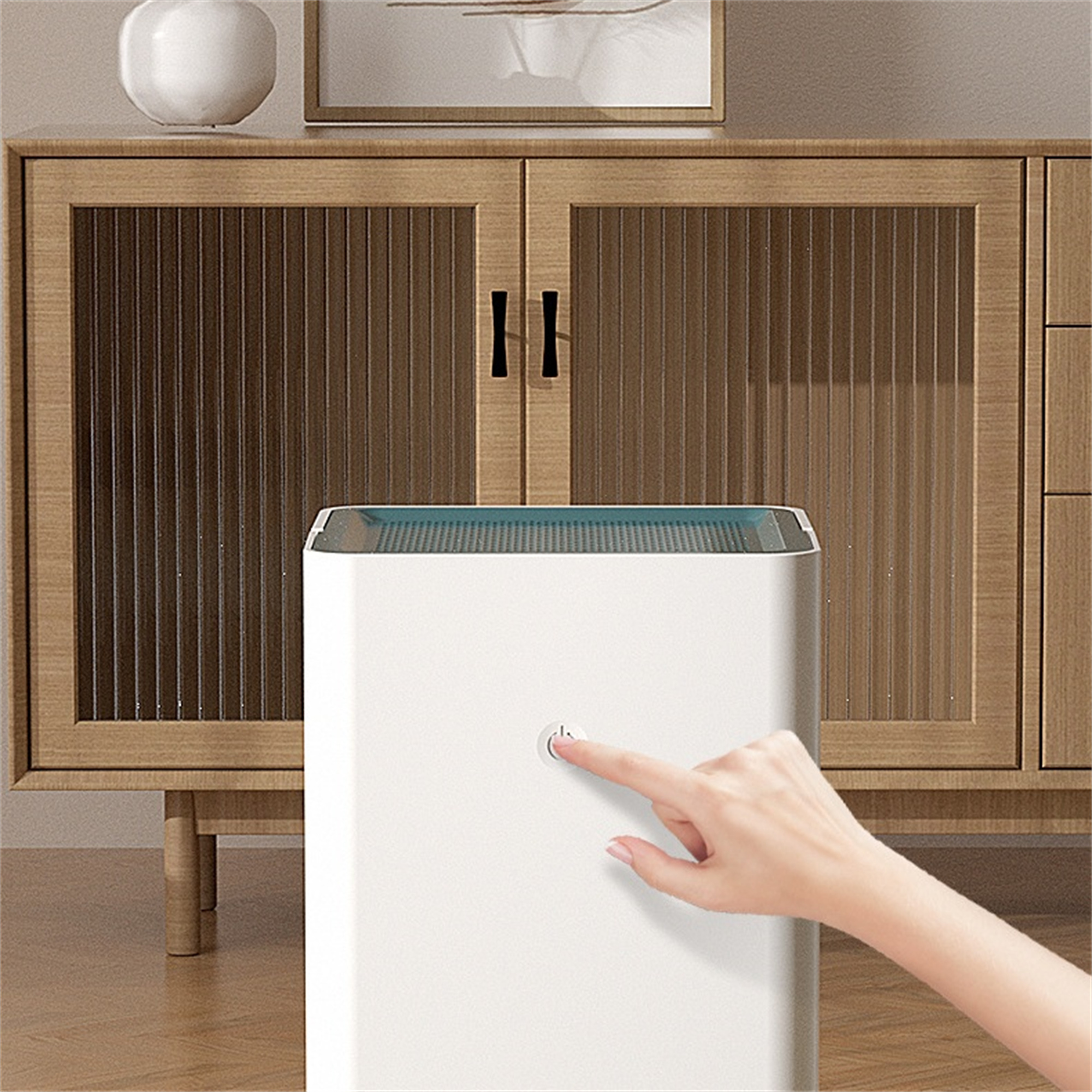 Eine Hand drückt die Einschalttaste eines weißen Luftreinigers. Ein Holzschrank befindet sich im Hintergrund.