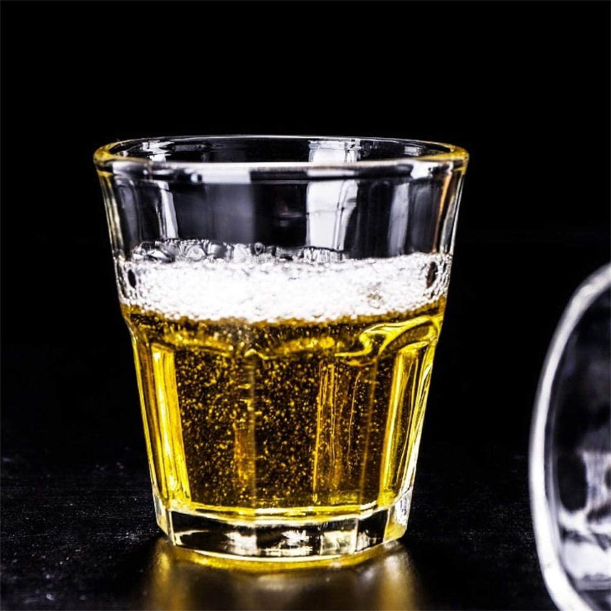 Ein Glas mit hellgelber Flüssigkeit und Schaum, möglicherweise Bier, vor schwarzem Hintergrund.