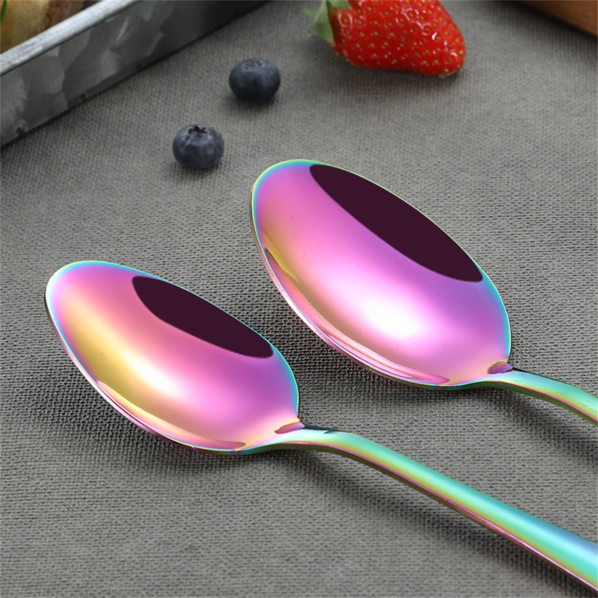 Zwei Löffel mit regenbogenfarbenem Metallic-Finish, mit Blaubeeren und einer Erdbeere.